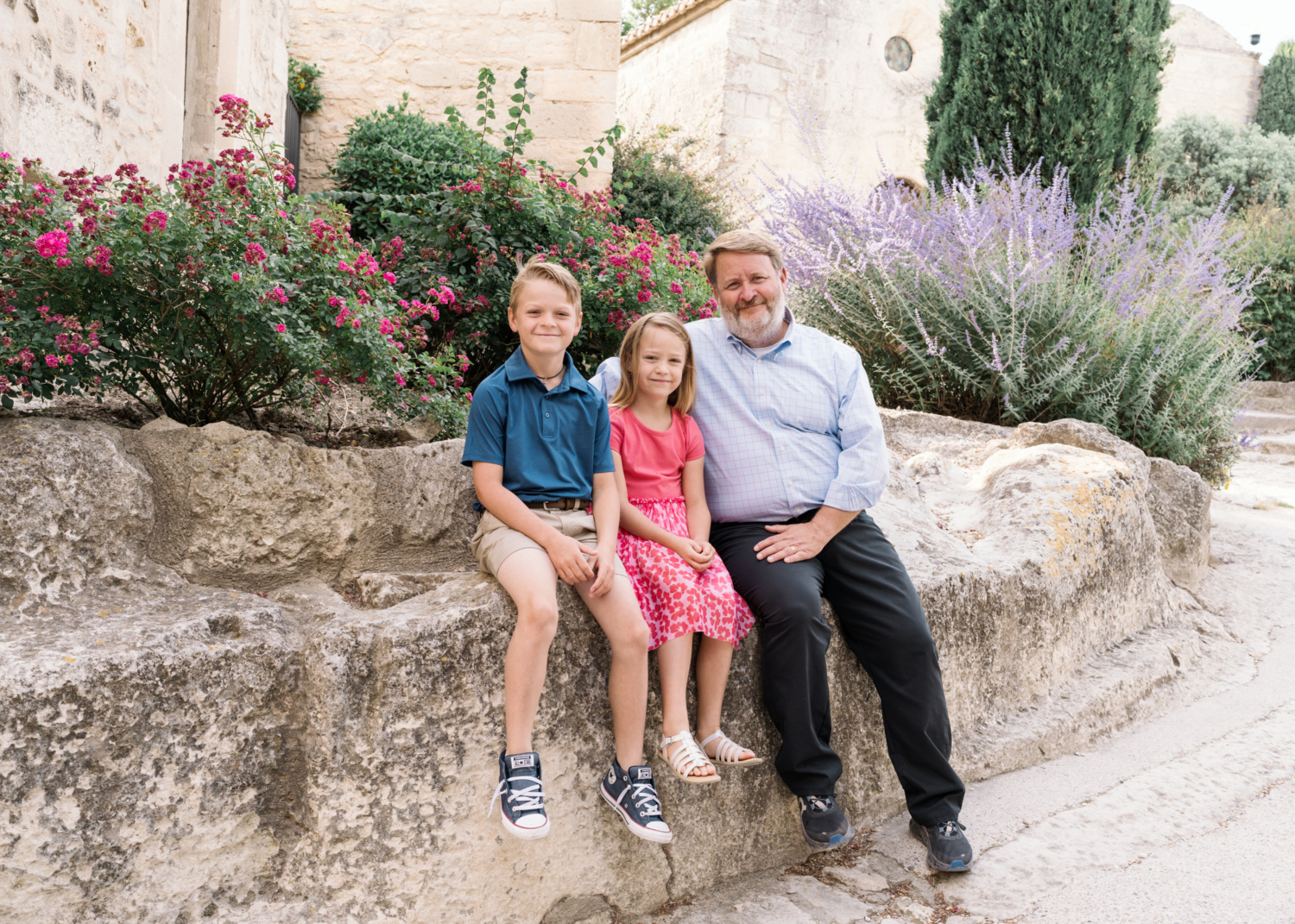 dad poses with his two children near flowers in les baux de provence france