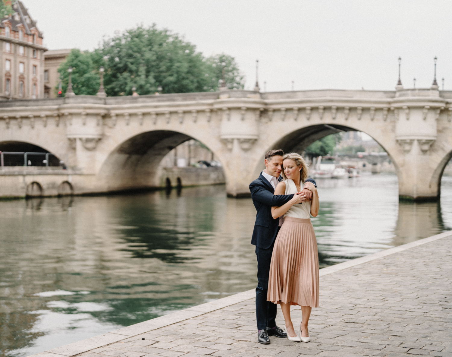 engaged couple embrace with view of pont neuf in paris