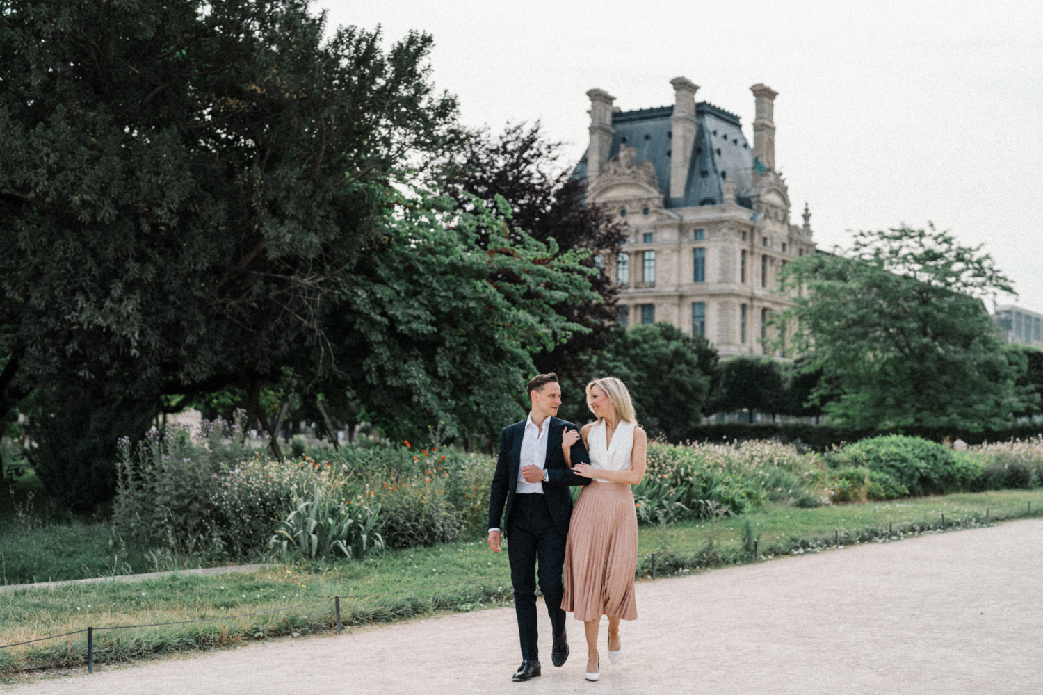engaged couple walk arm in arm in garden in paris