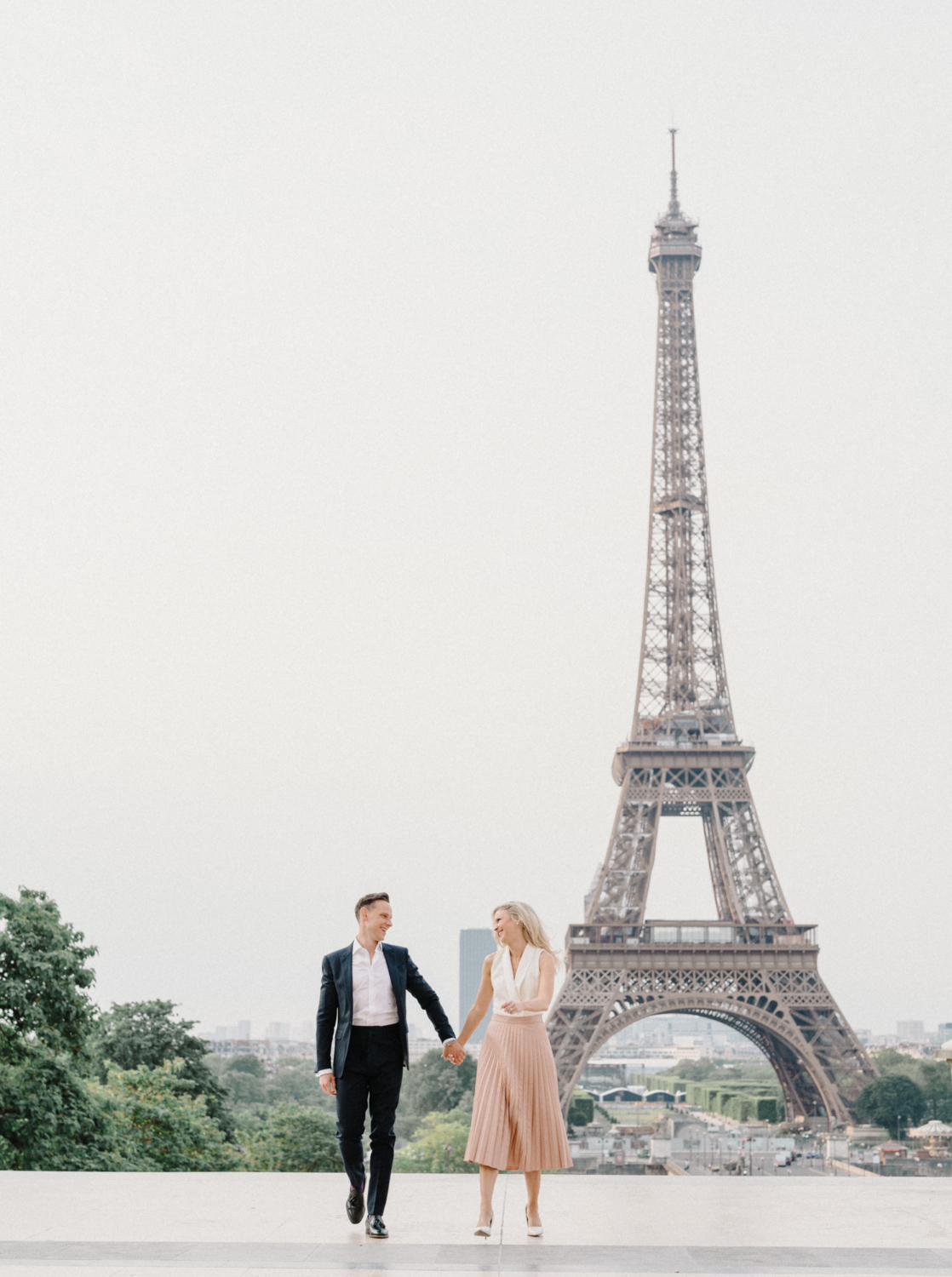 engaged couple laugh and walk with view of eiffel tower paris