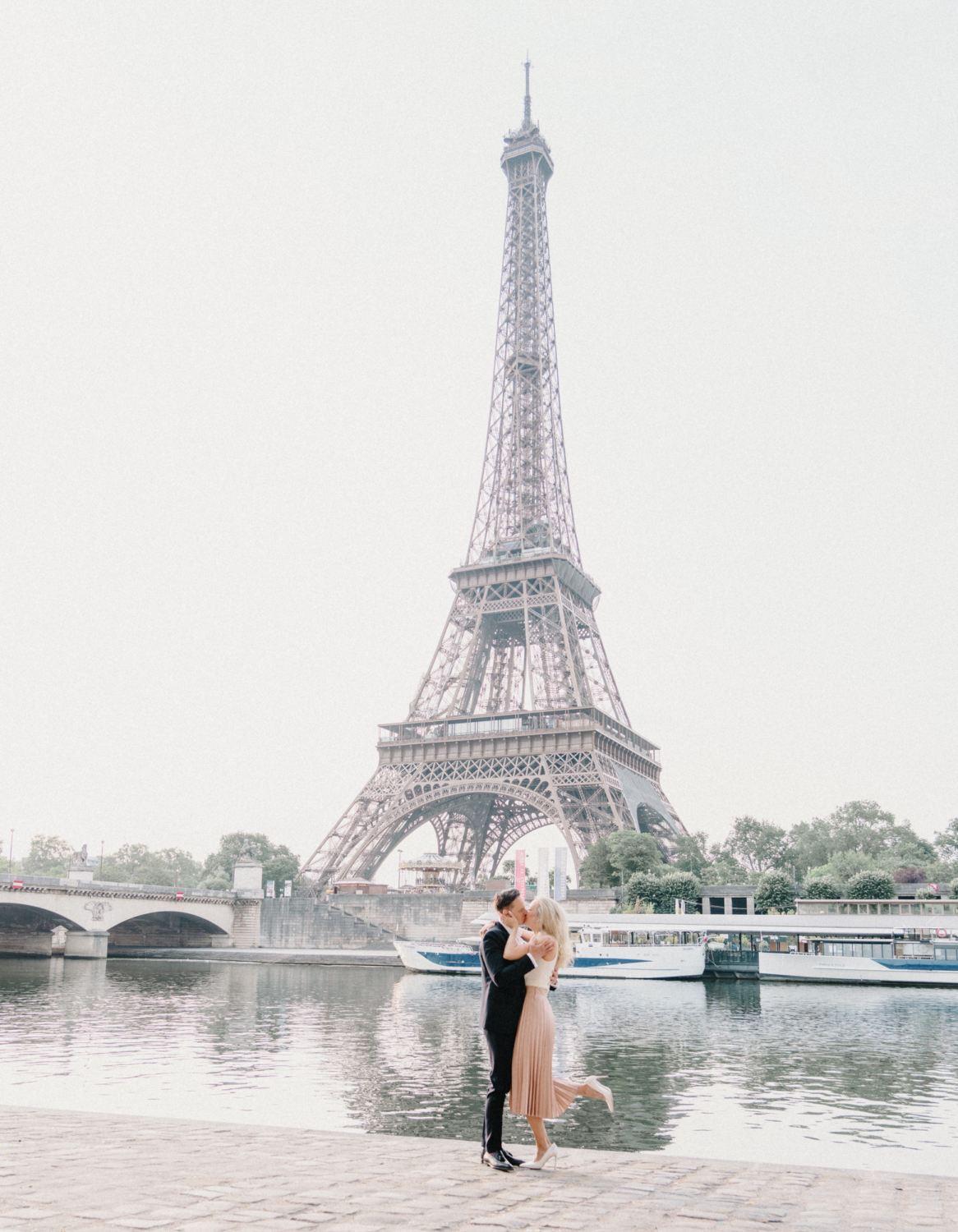 engaged couple embrace and kiss with view of eiffel tower in paris