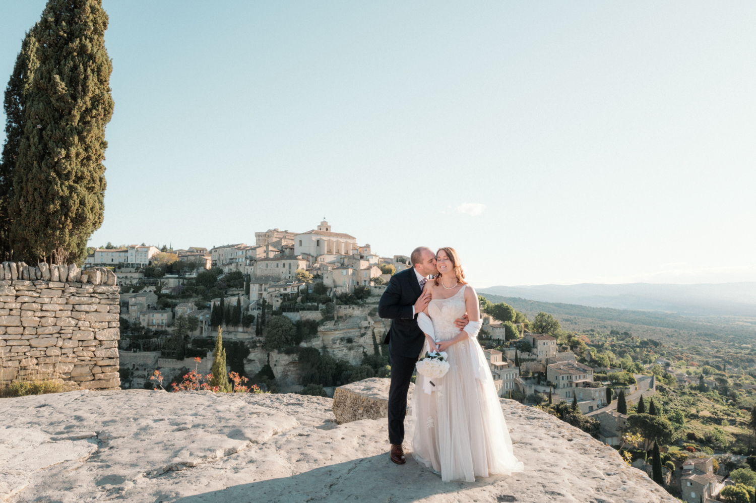 groom kissing bride with view of gordes village