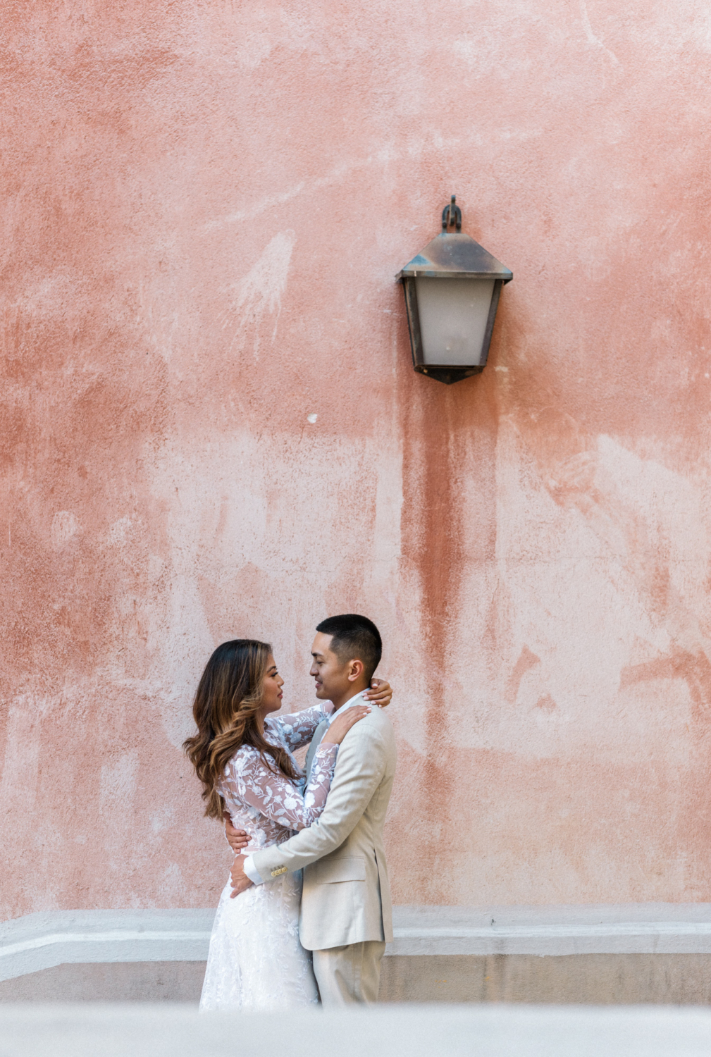 engaged couple embrace next to pink wall in nice france