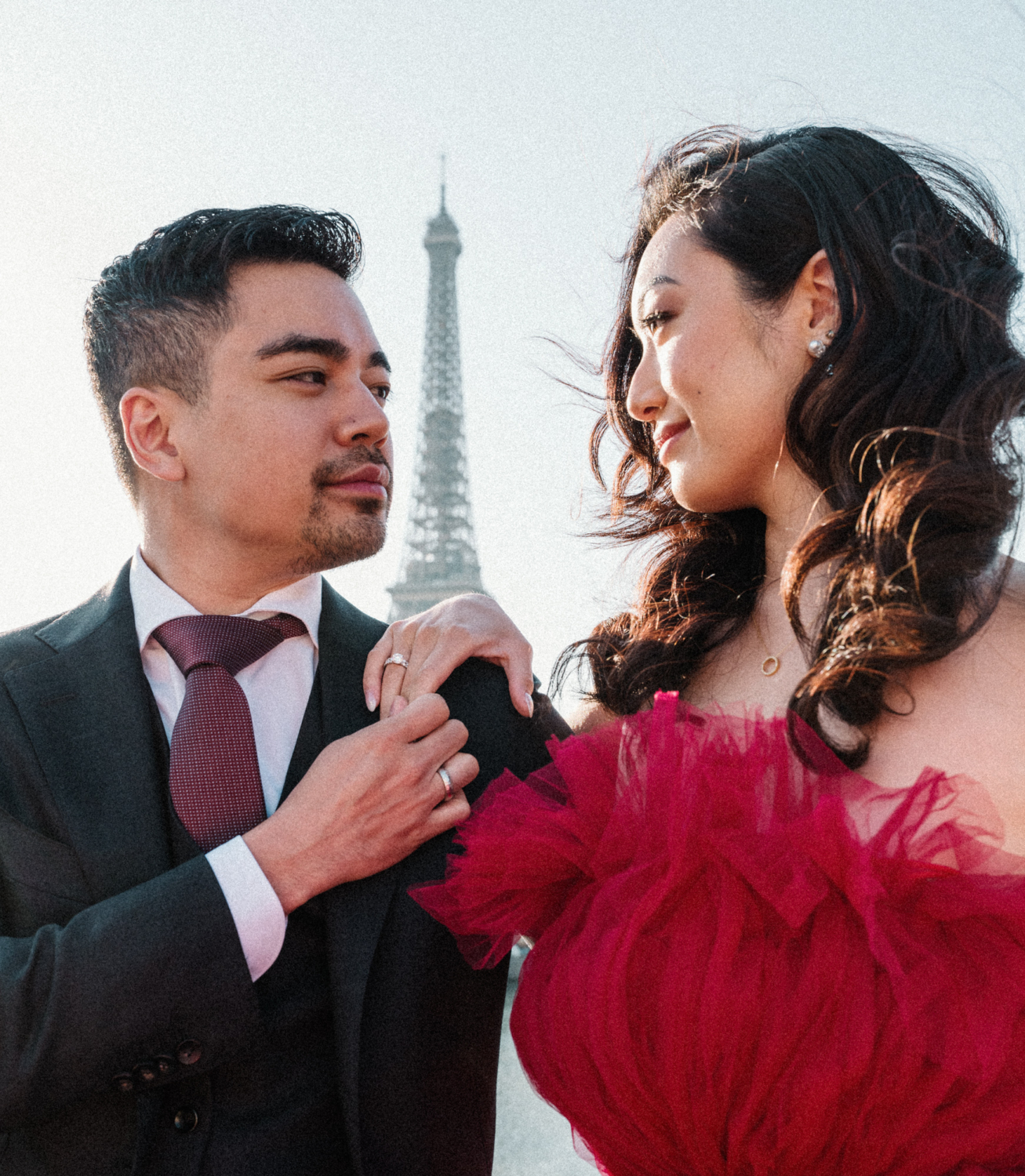 asian couple pose in suit and red gown with view of eiffel tower