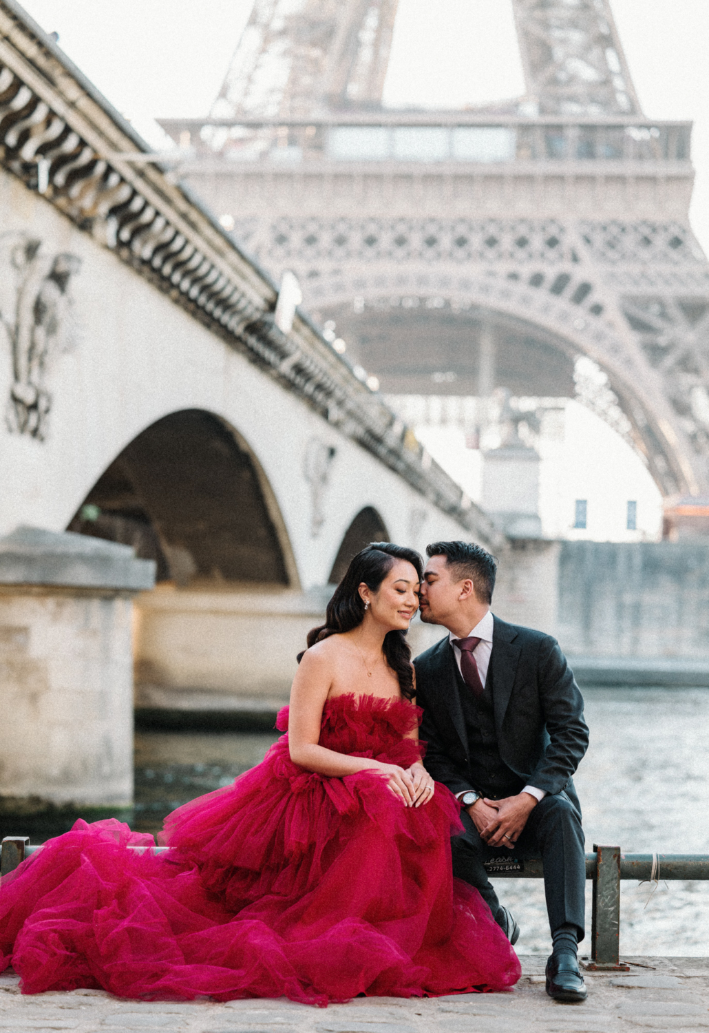 man whispers in ear of woman wearing red gown at eiffel tower