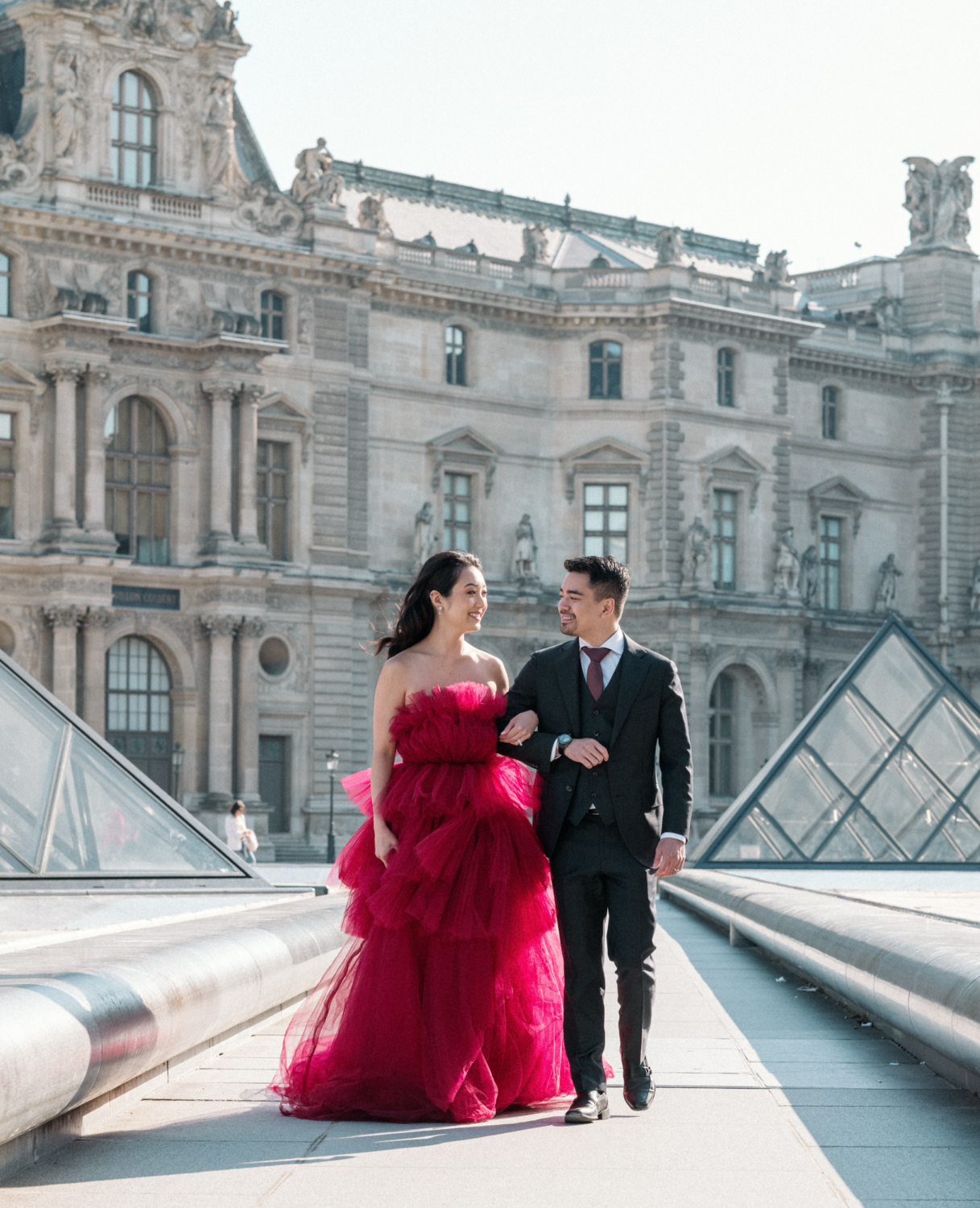 asian couple walk arm in arm with louvre museum in background