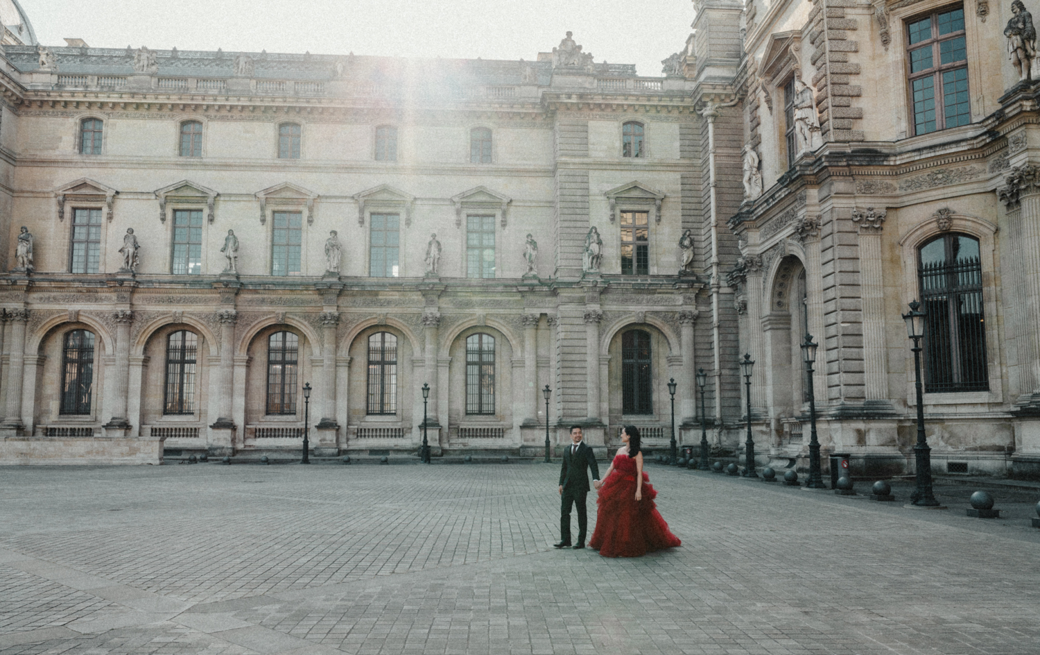 asian couple walk through louvre museum courtyard in paris