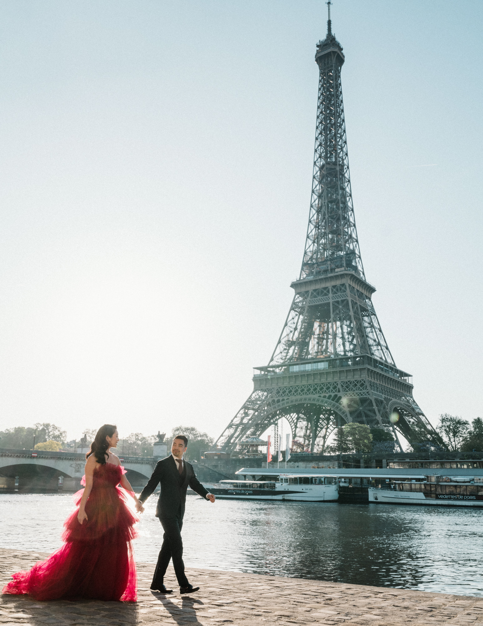 asian couple walk along seine river in paris with view of eiffel tower