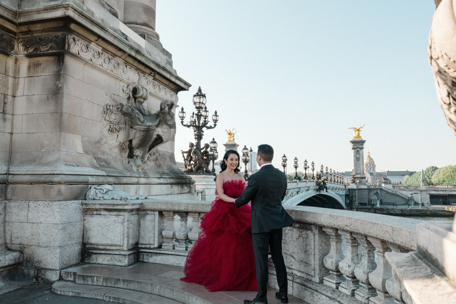 asian couple hold hands and laugh on bridge in paris