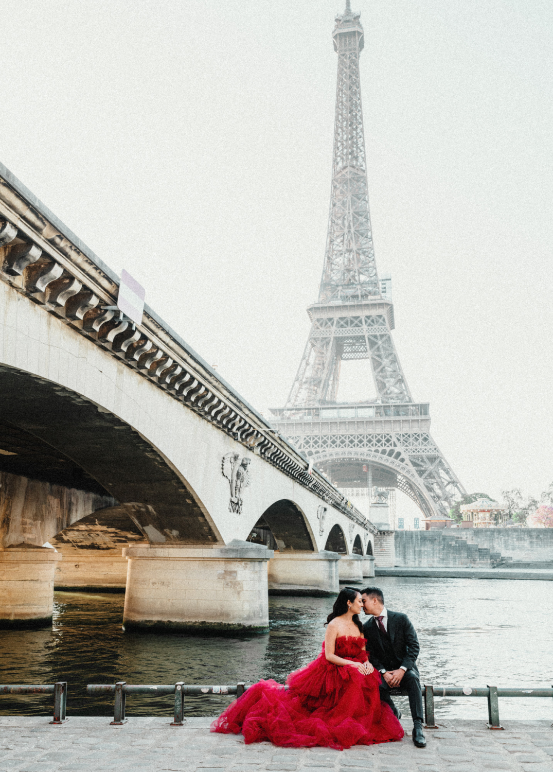 asian couple sit with red gown and suit and eiffel tower in background