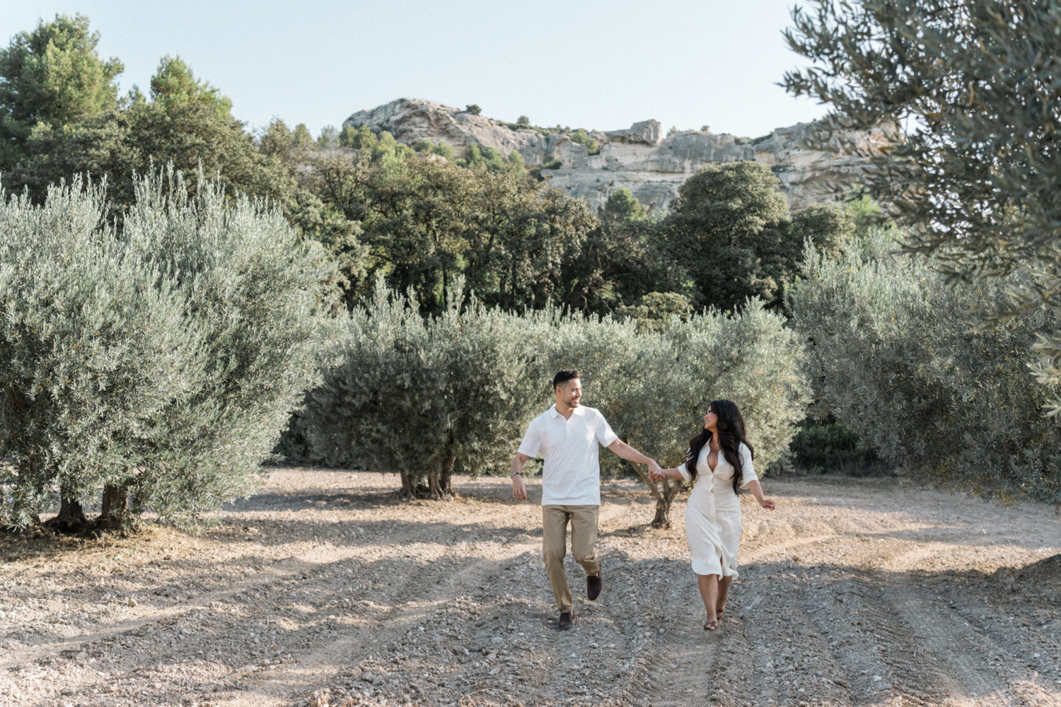 smiling couple run in olive grove with mountain in background