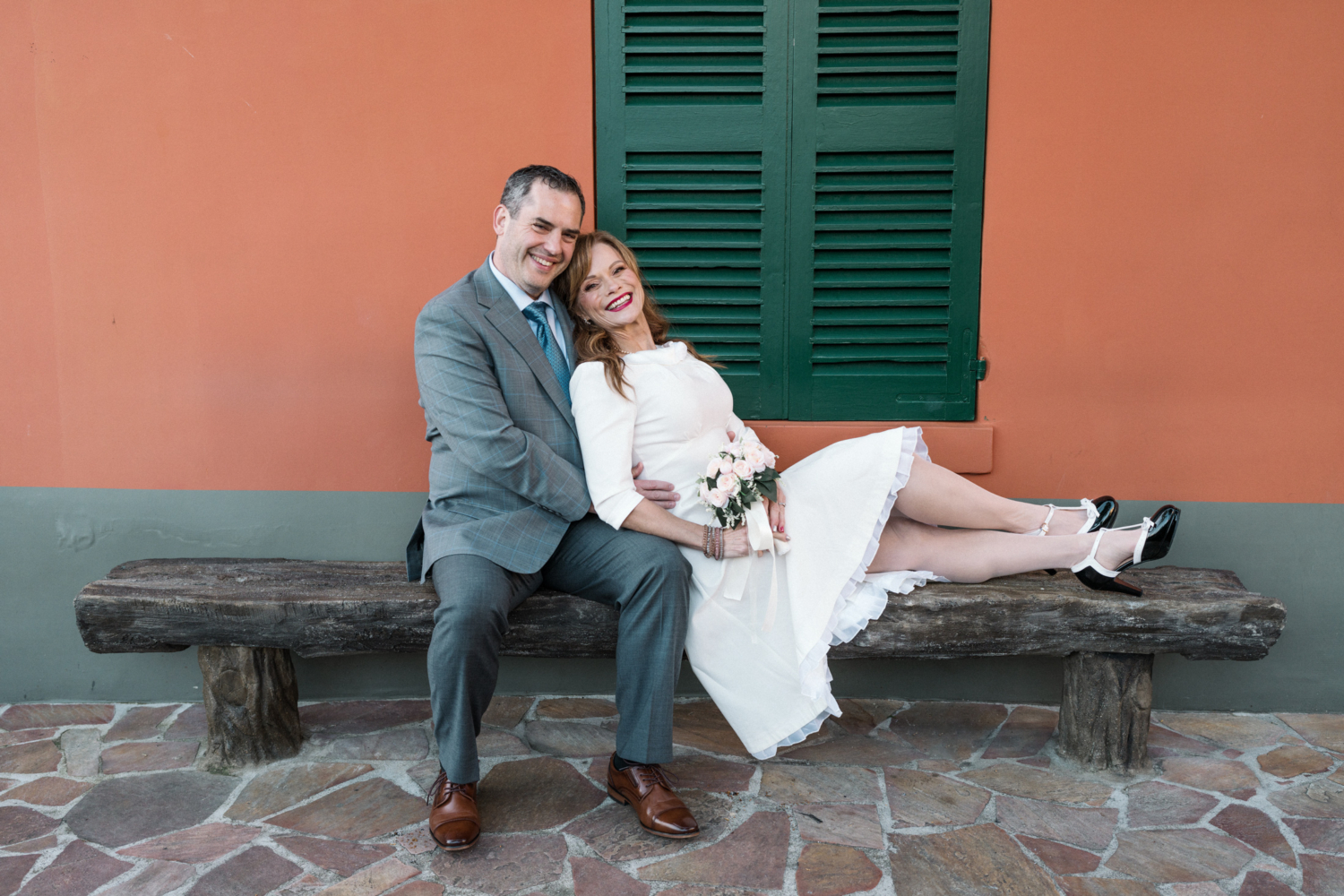 newlyweds smile as they sit on bench in paris