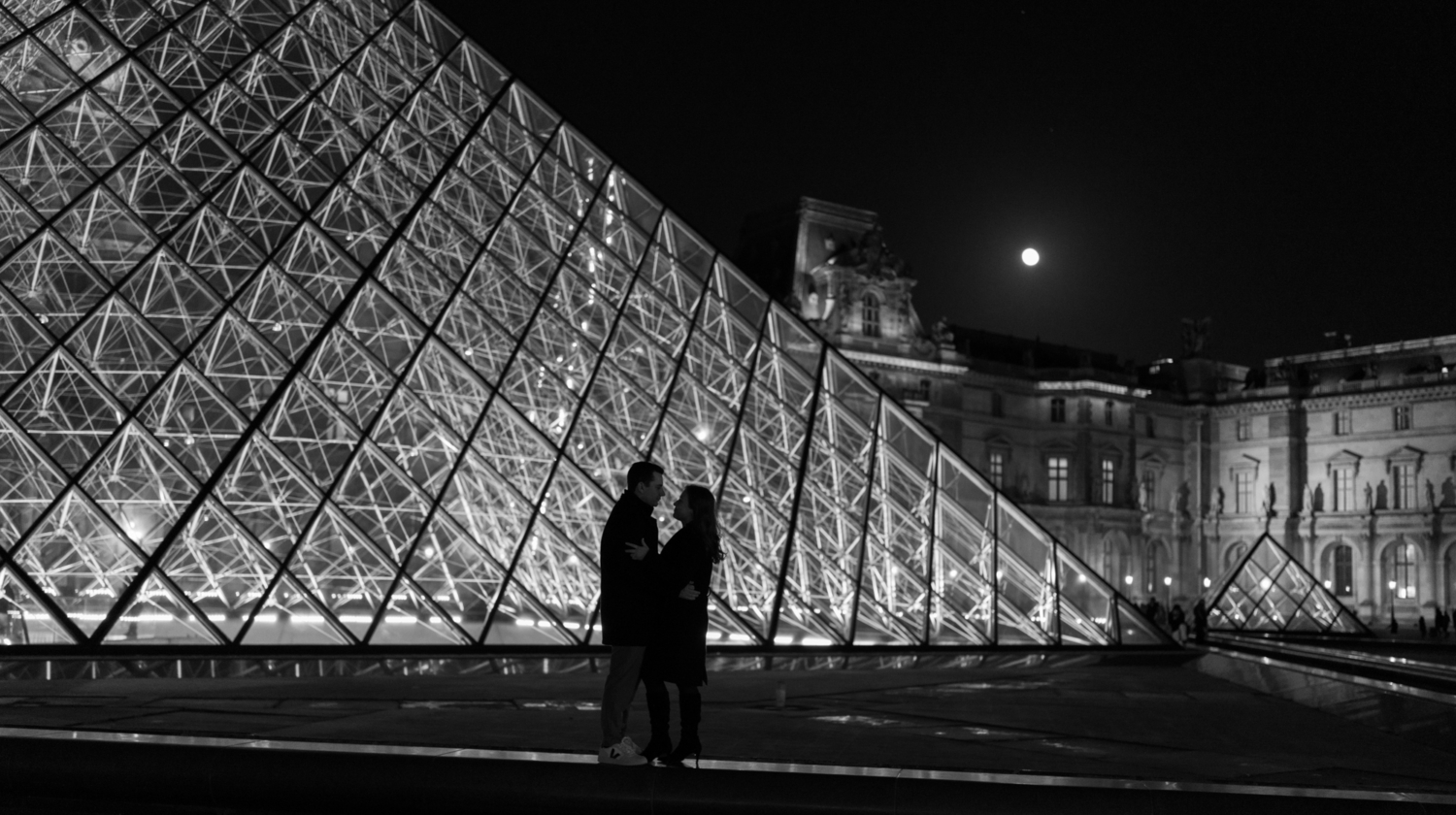 engaged couple embrace at night at the pyramid of the louvre paris