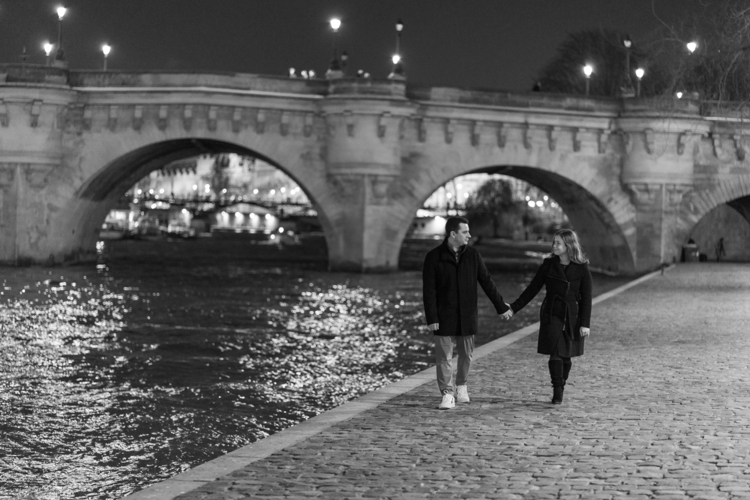 engaged couple walk hand in hand next to seine river in paris