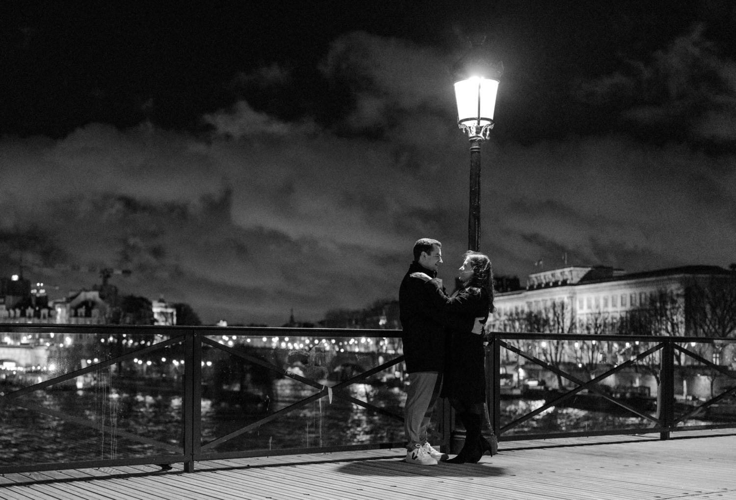 engaged couple embrace on pont des arts in paris at night