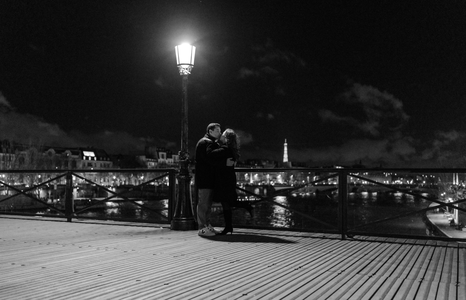 engaged couple kiss on pont des arts at night with view of eiffel tower