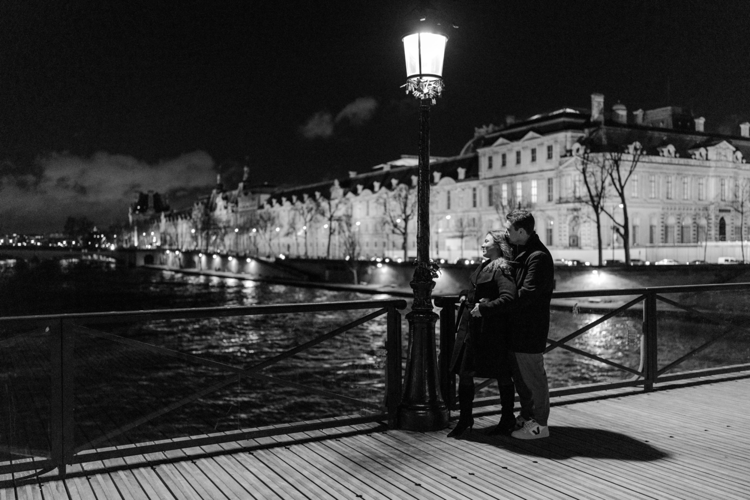 engaged couple embrace on pont des arts at night in paris