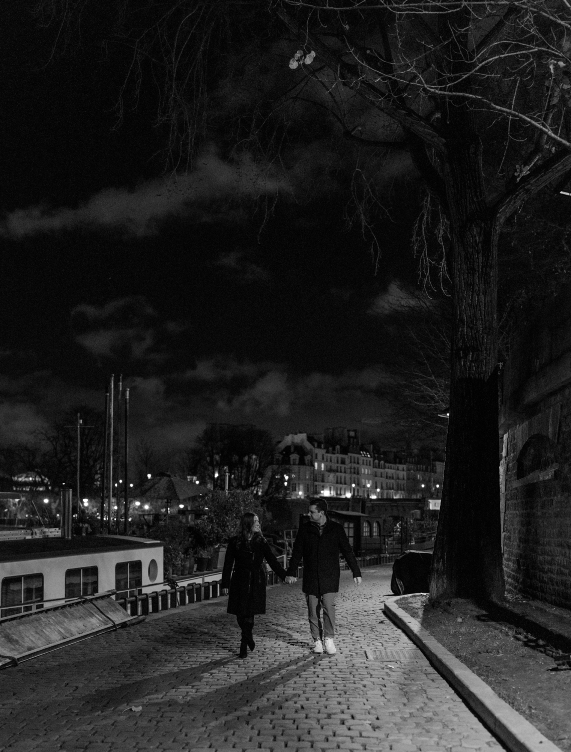 engaged couple walk along seine river at night in paris