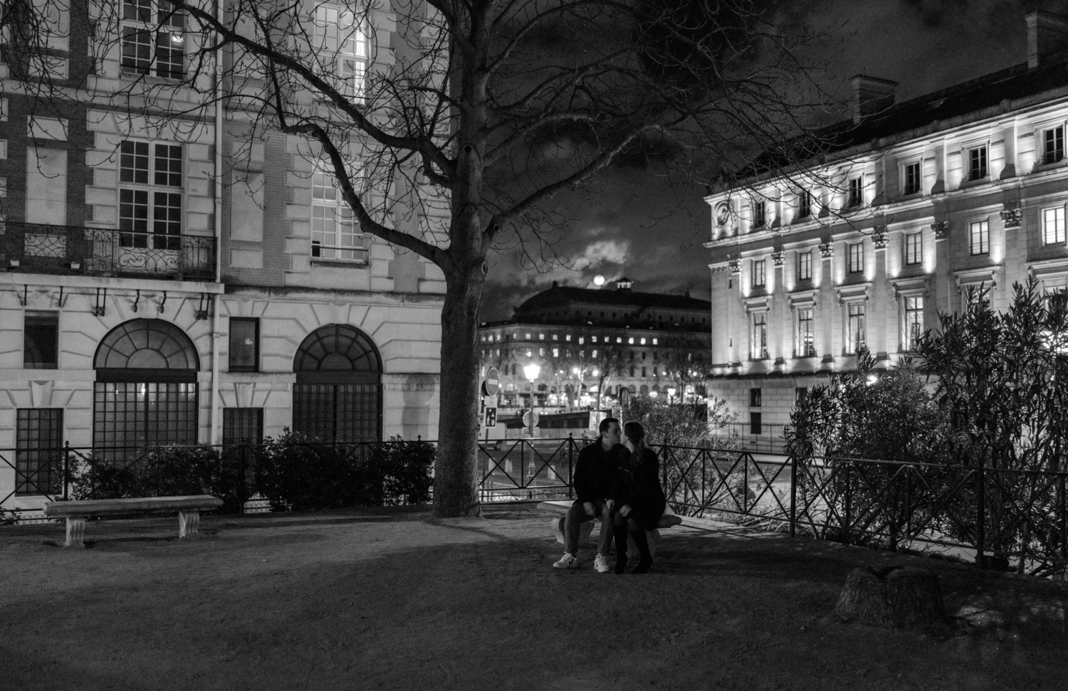 engaged couple sit on bench at night under full moon in paris