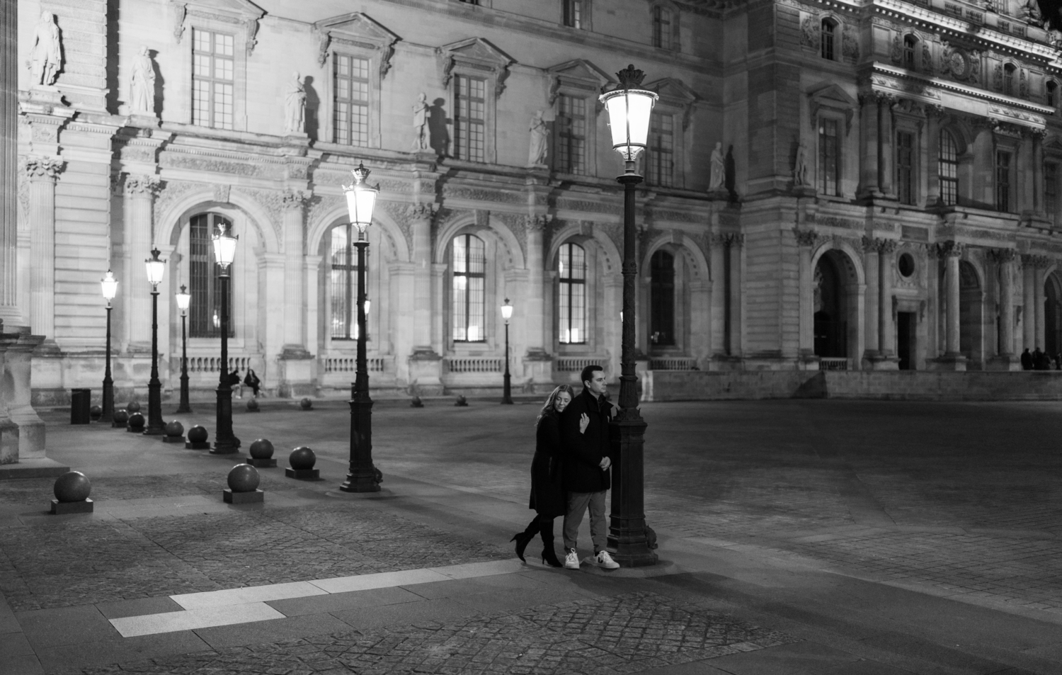 engaged couple embrace at the louvre museum in paris at night