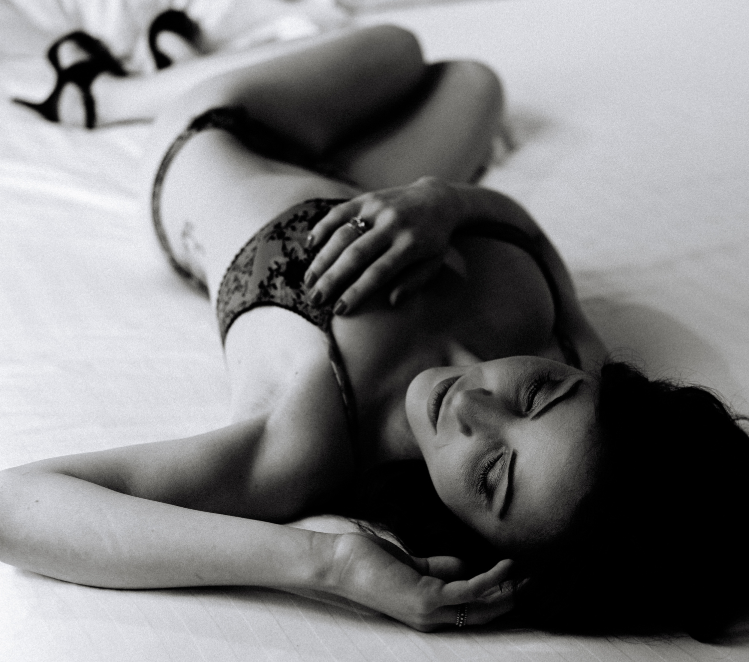 woman lays on bed wearing lingerie and high heels during boudoir photoshoot in paris