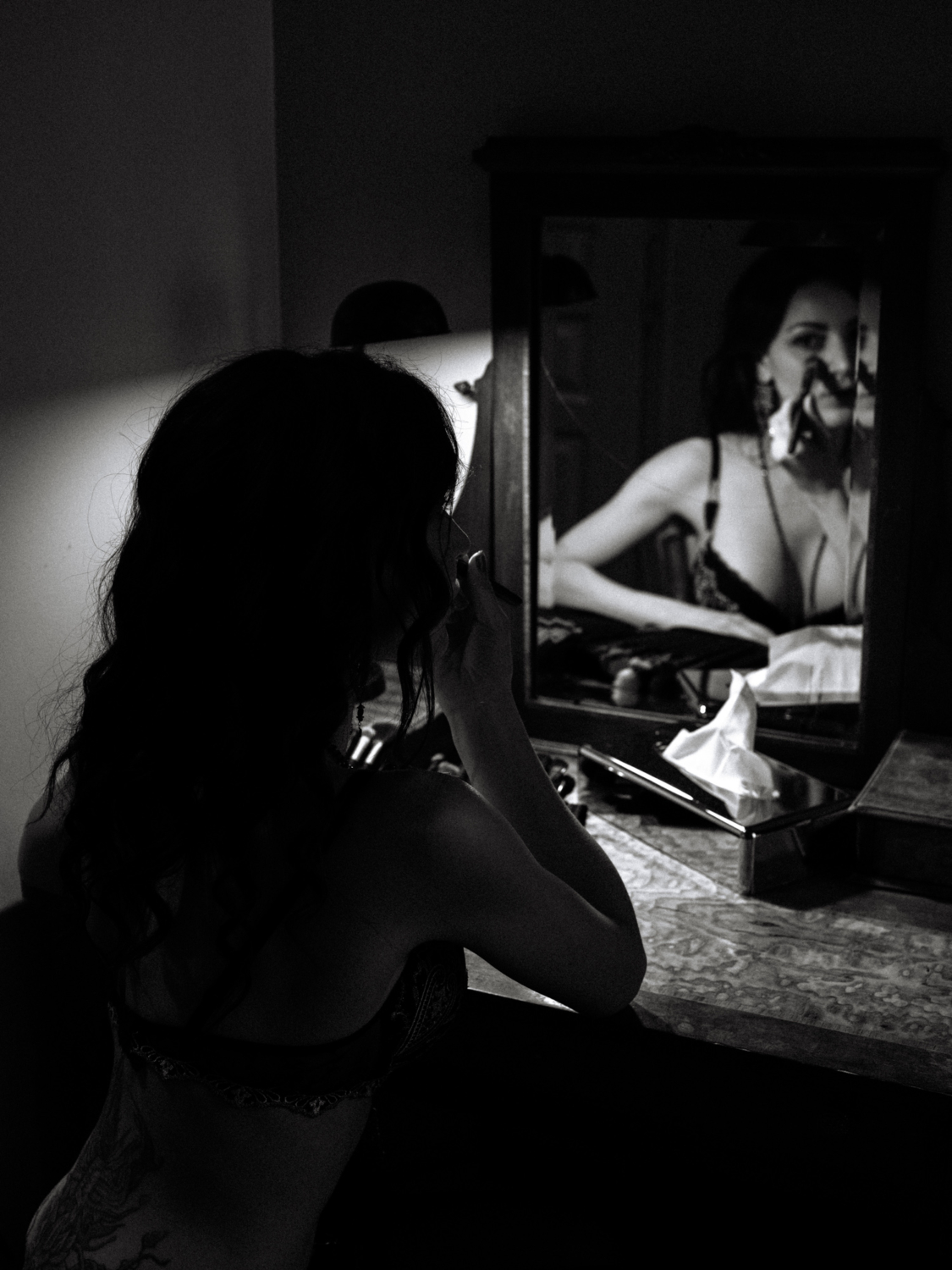 woman applies makeup in mirror during boudoir photoshoot in paris