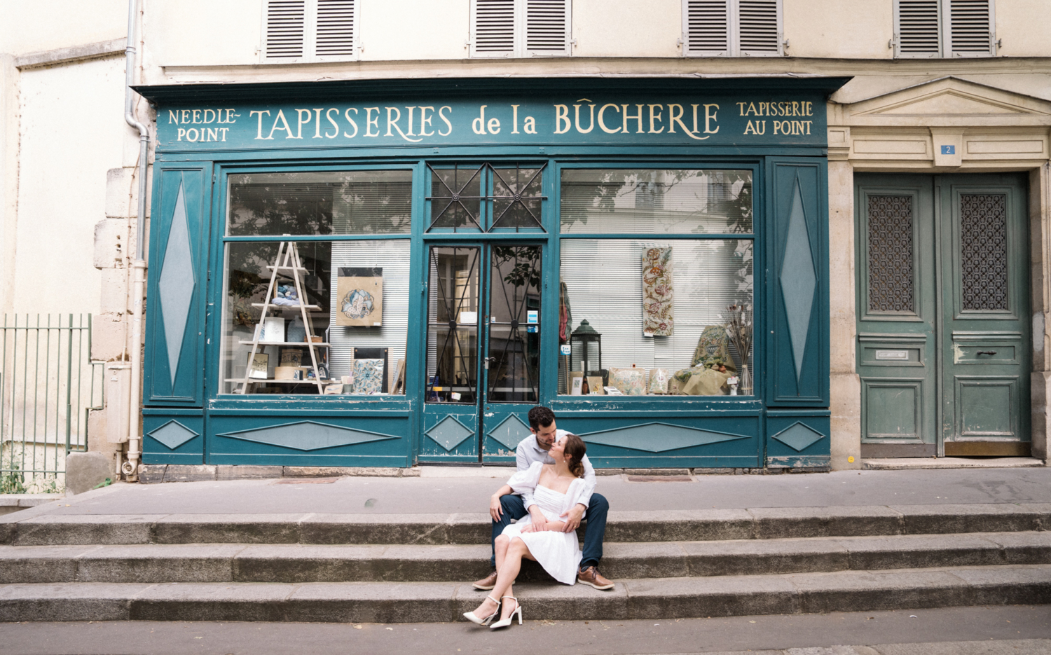 engaged couple sit on steps in front of cute building in pris