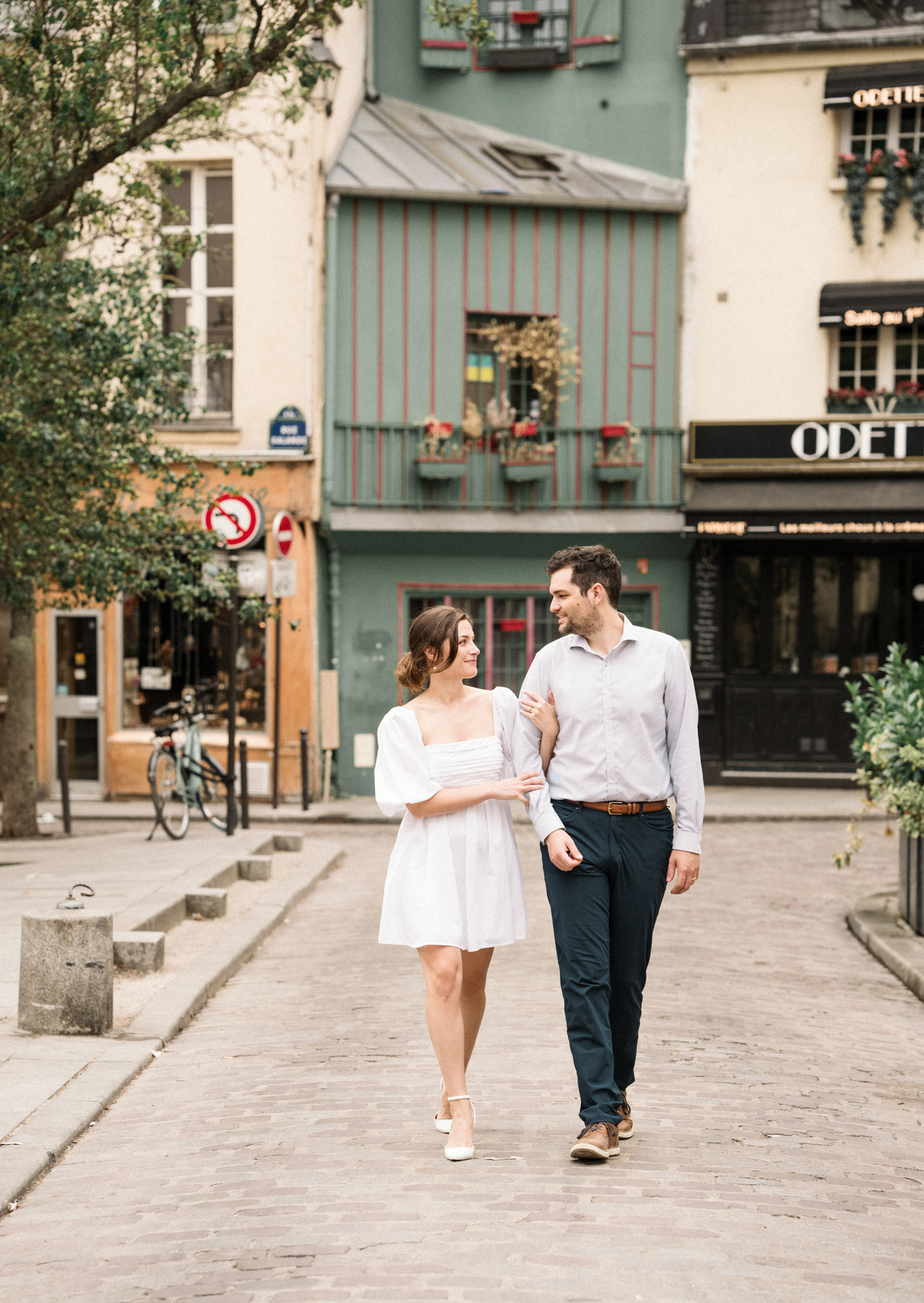 engaged couple walk arm in arm in charming neighborhood in paris