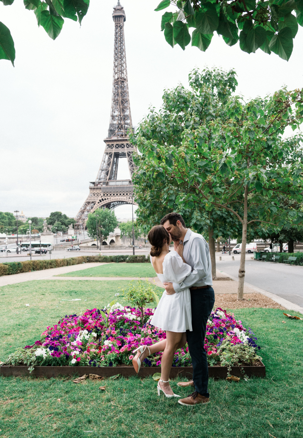 engaged couple share a passionate kiss in garden with view of eiffel tower