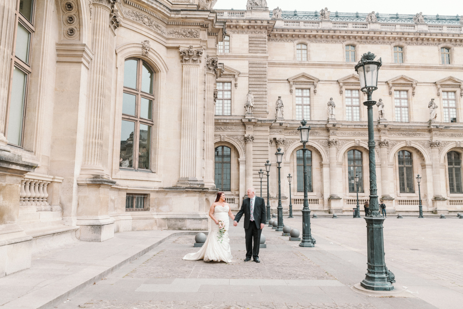 bride and groom hold hands at the louvre in paris