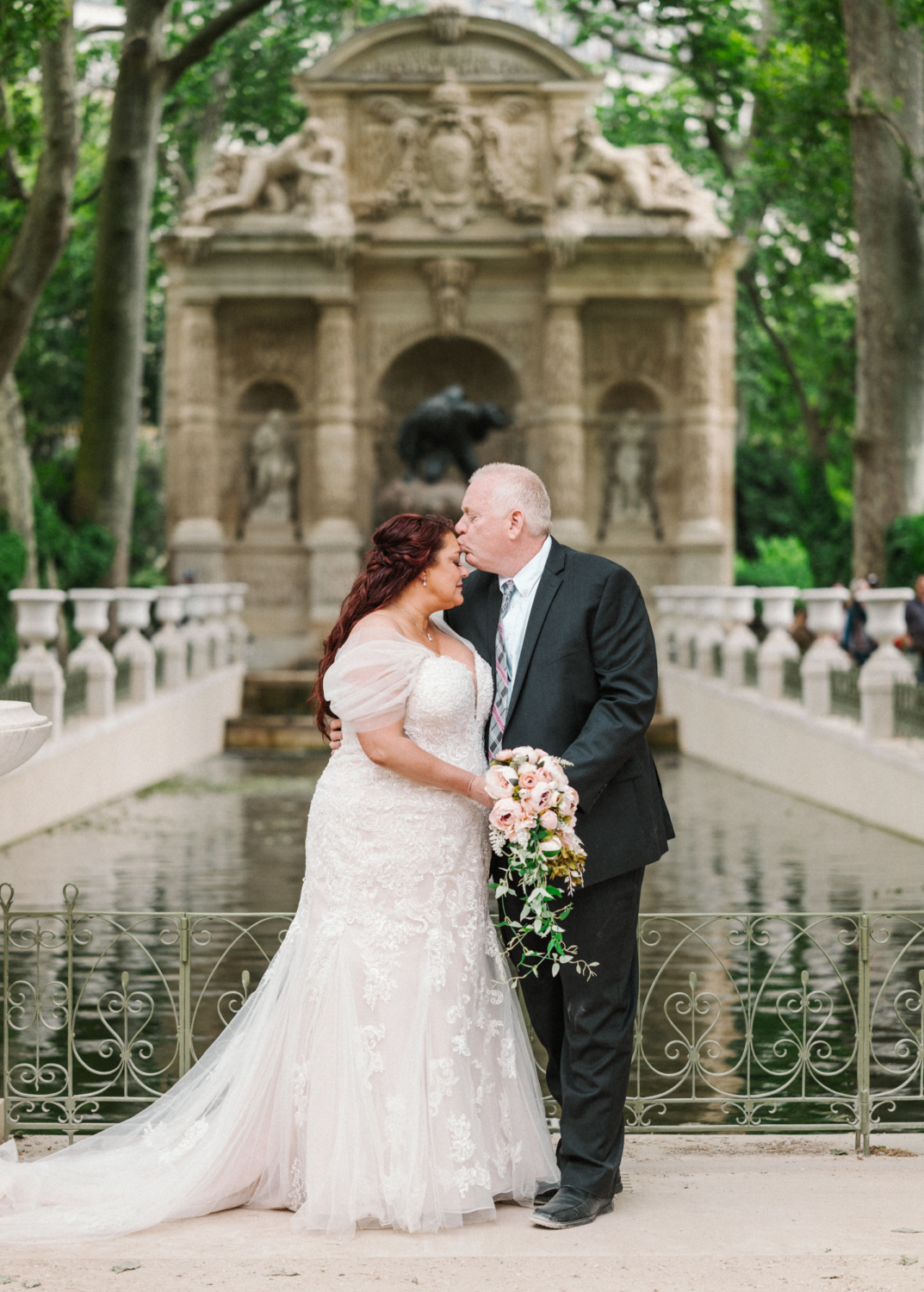 groom kisses bride on forehead at medici fountain in luxembourg gardens