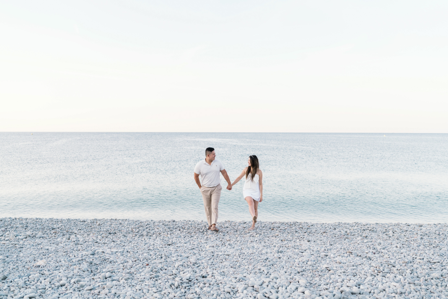 newlyweds hold hands and smile as they walk on the beach in nice france