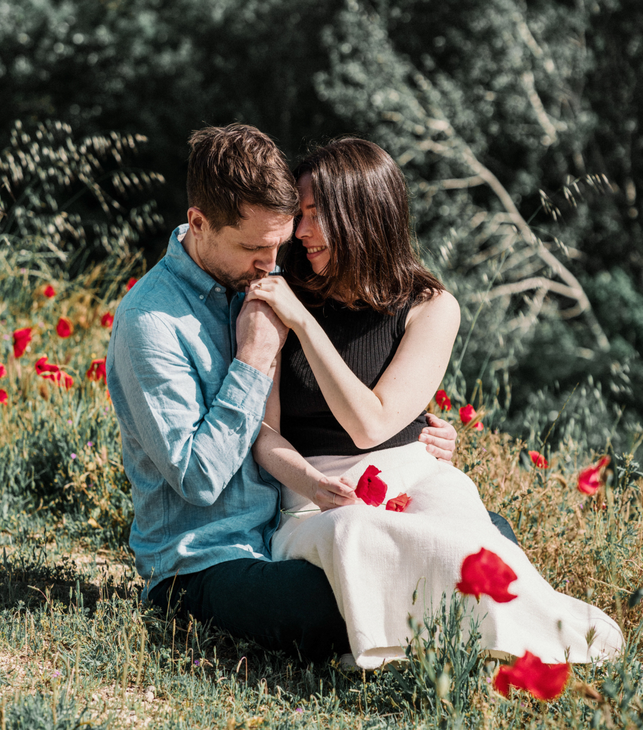 man kisses woman's hand in poppy field
