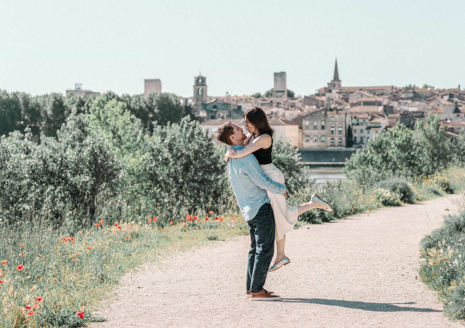 man lifts woman in air with arles in background