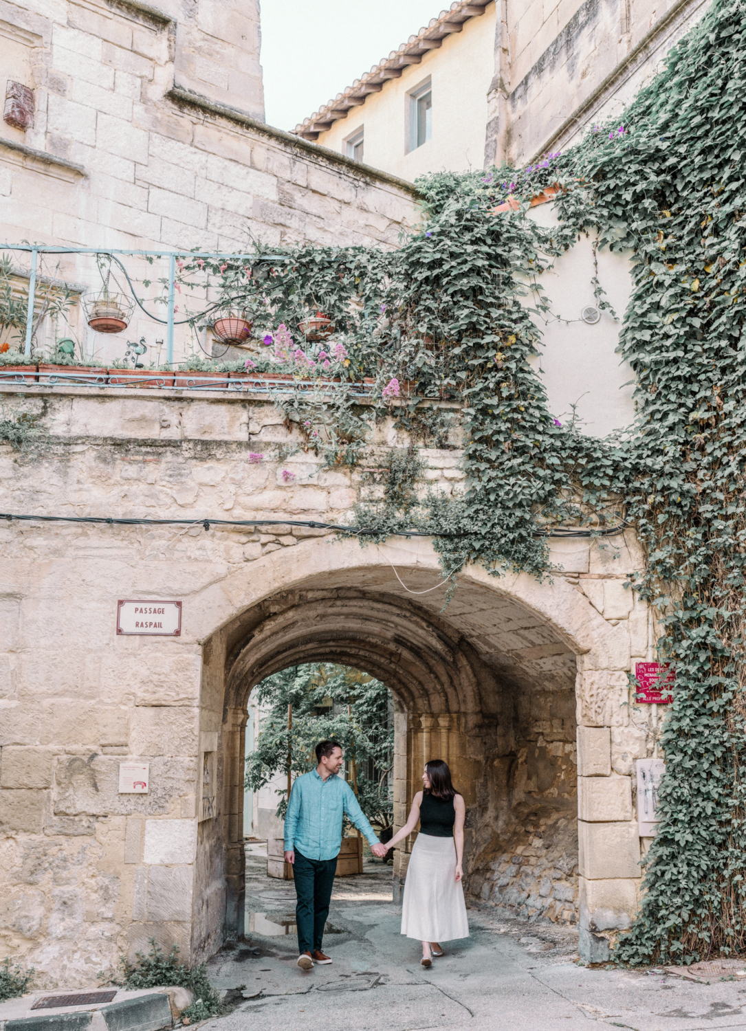 engaged couple walk hand in hand under arch in arles