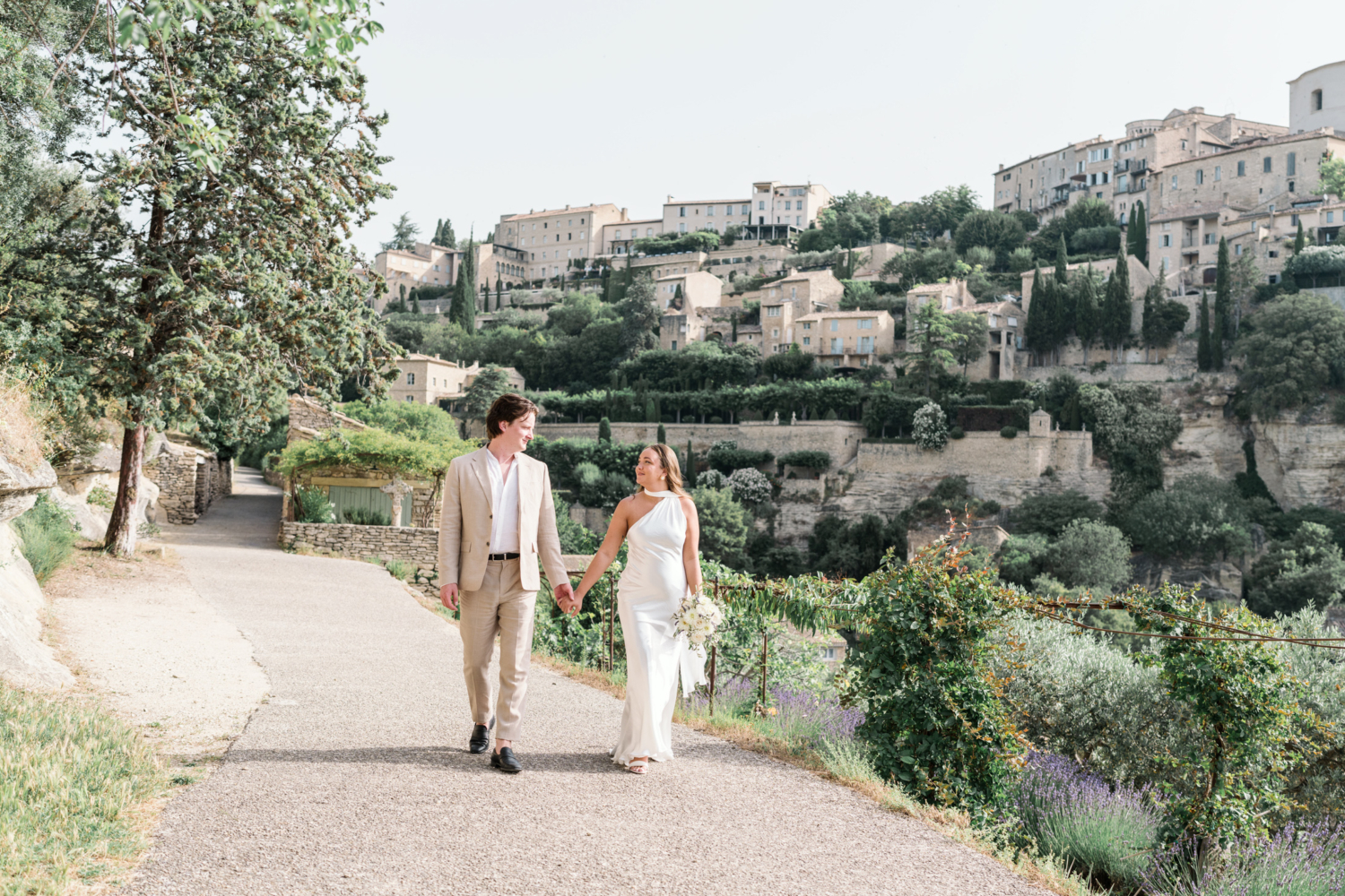 bride and groom walk hand in hand in gordes france