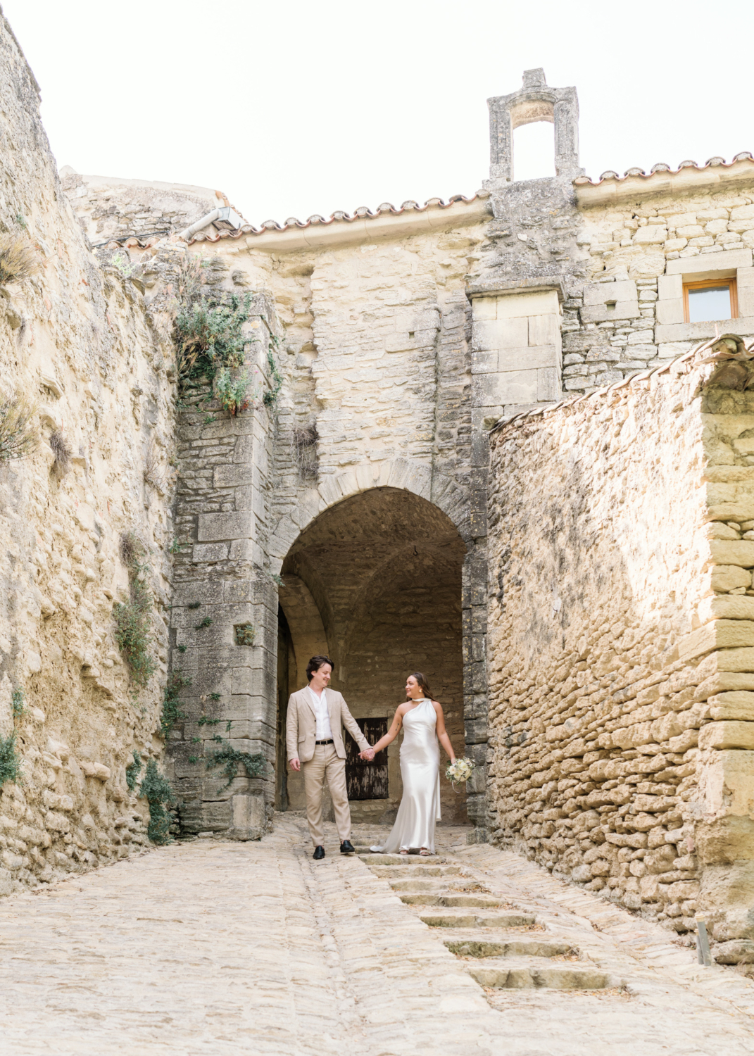 bride and groom walk hand in hand in gordes france