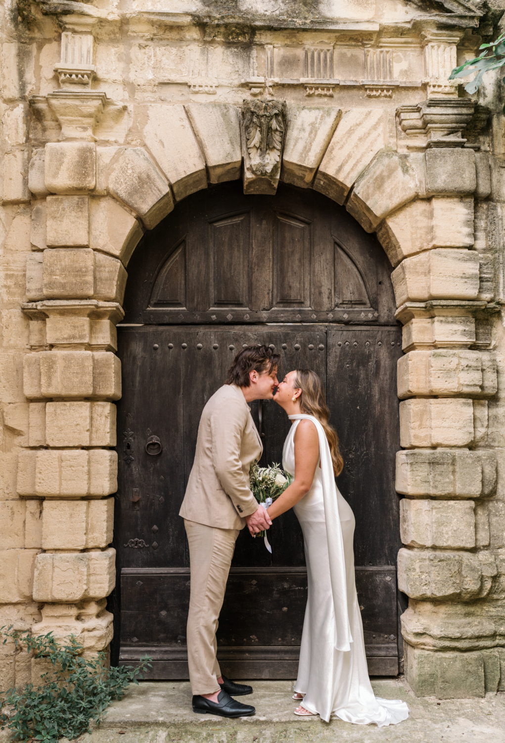 bride and groom kiss in front of brown door in gordes france