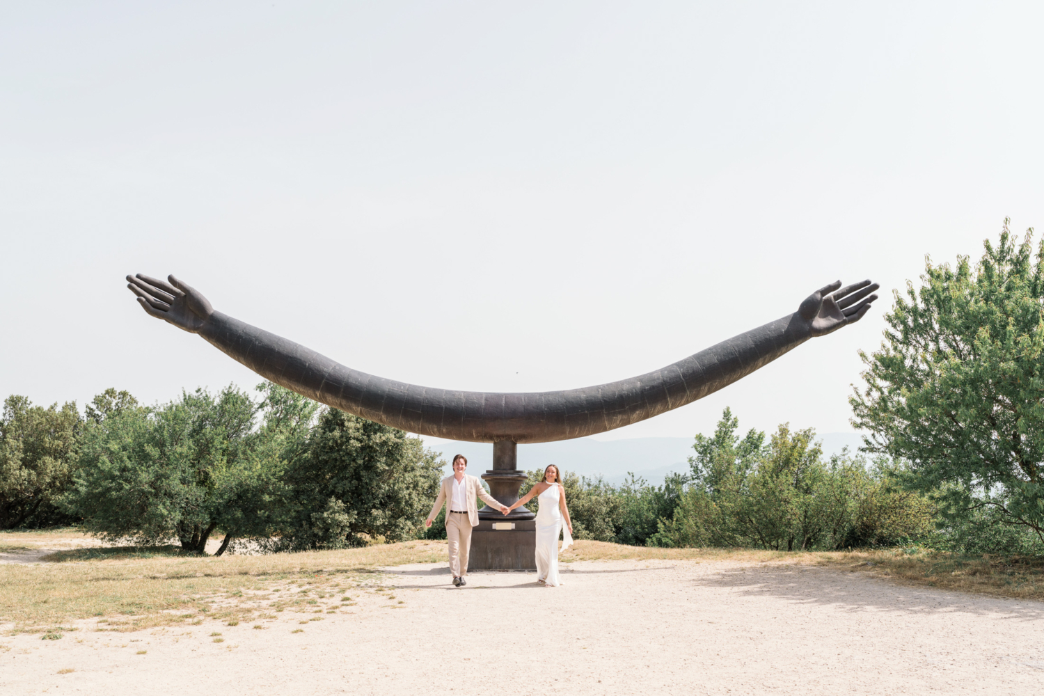 bride and groom walk under hand sculpture in lacoste france