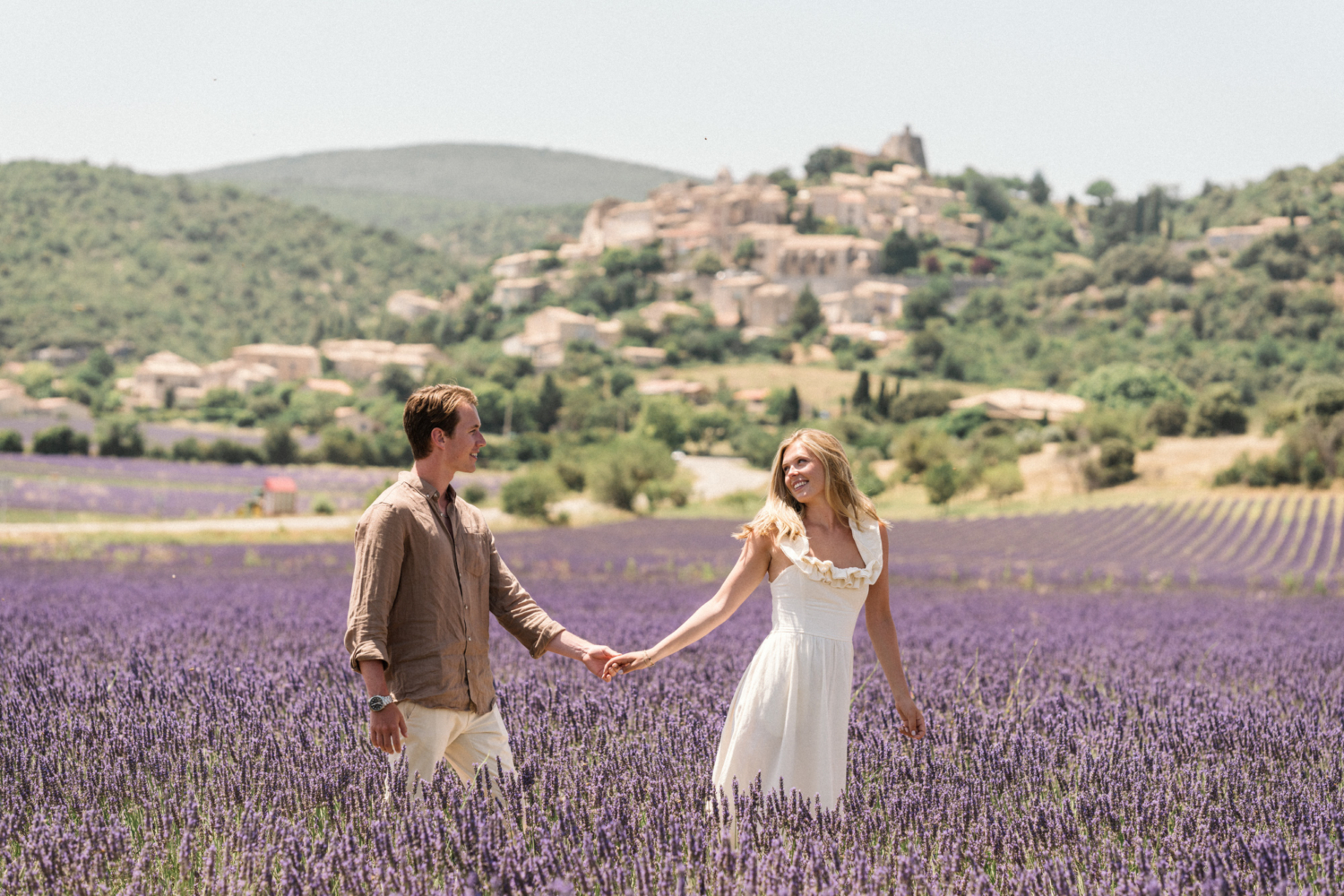 couple walk hand in hand in lavender field with medieval village