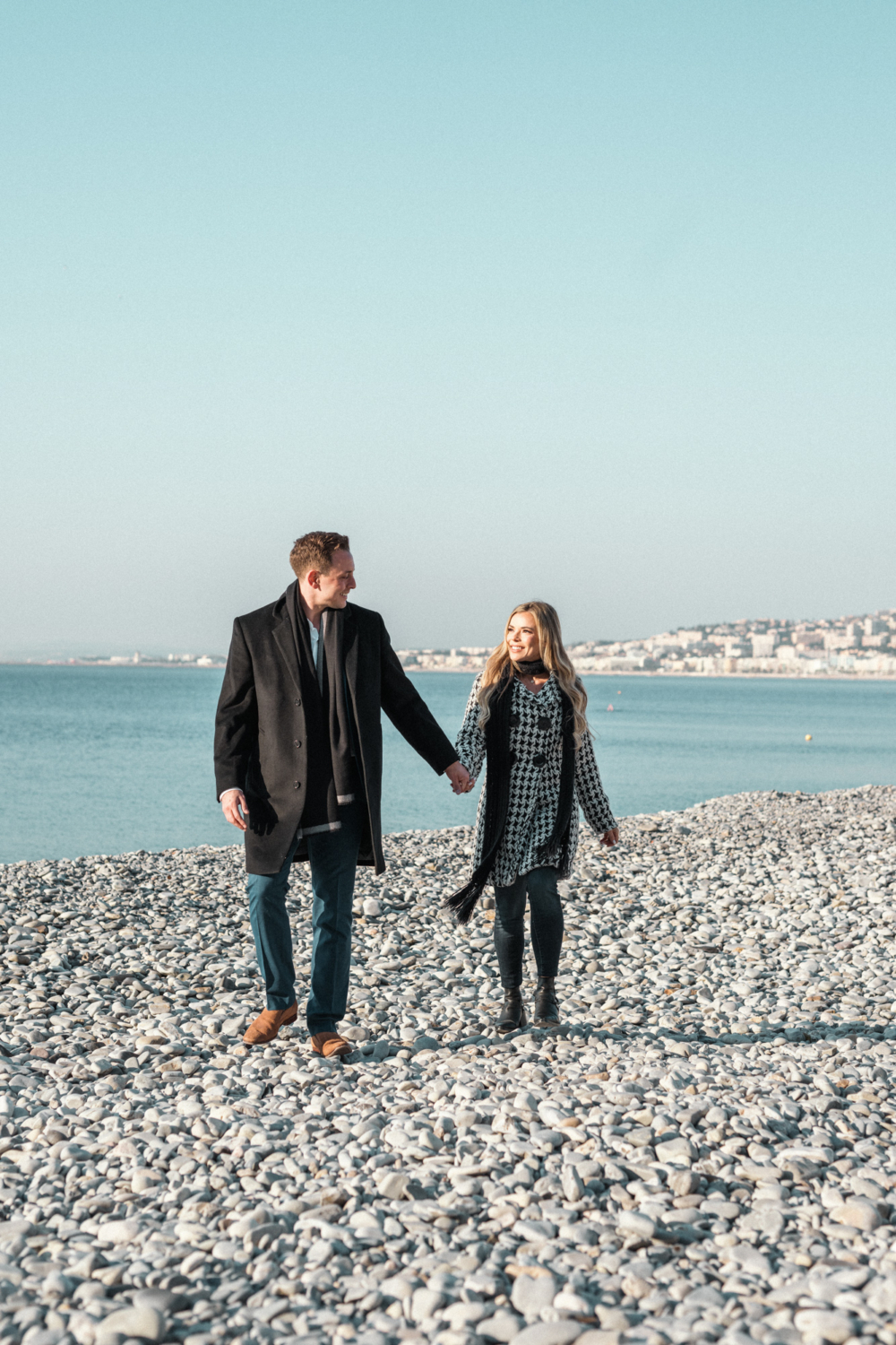 couple in winter coats run on the beach in nice france