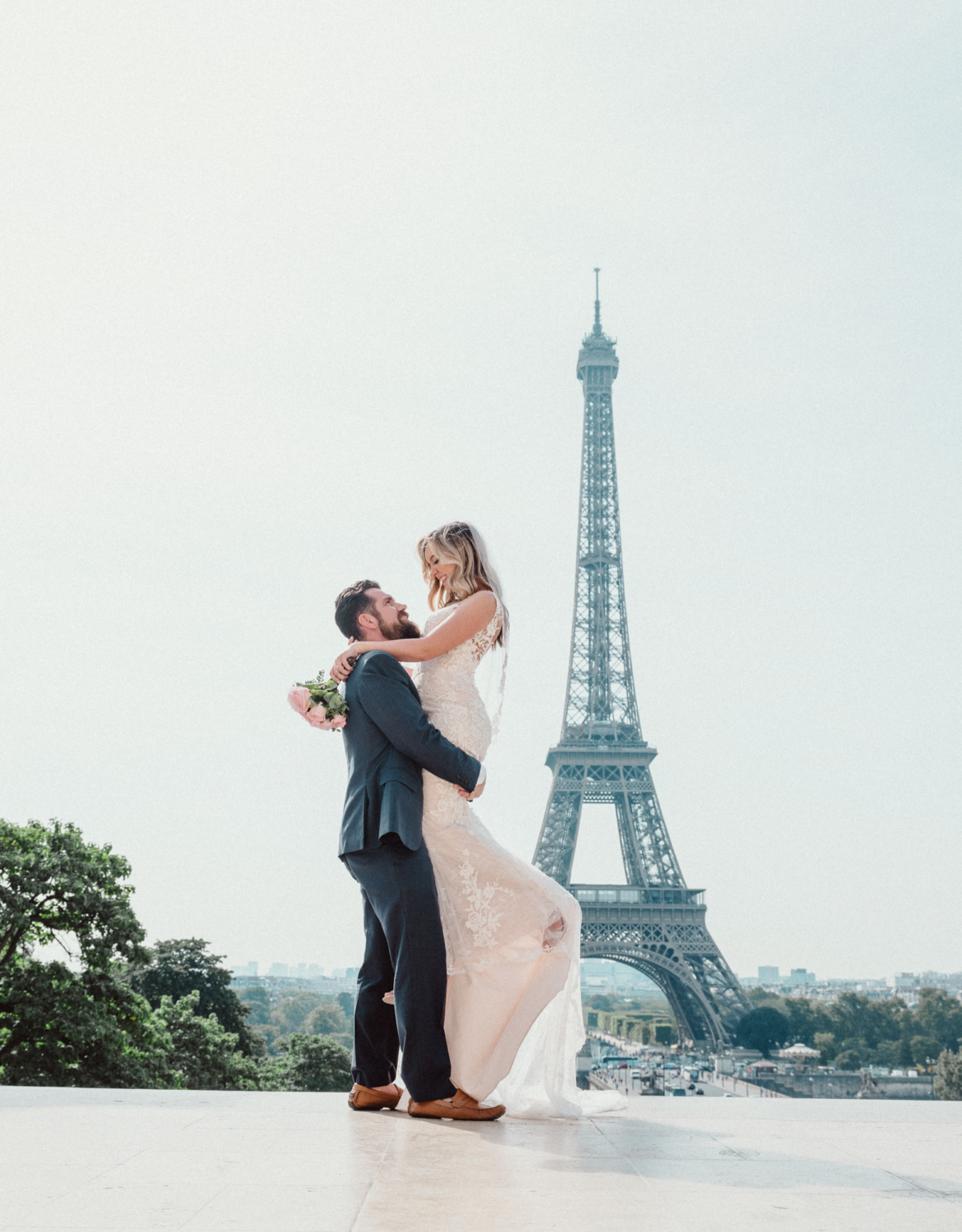 groom lifts bride in air with view of eiffel tower