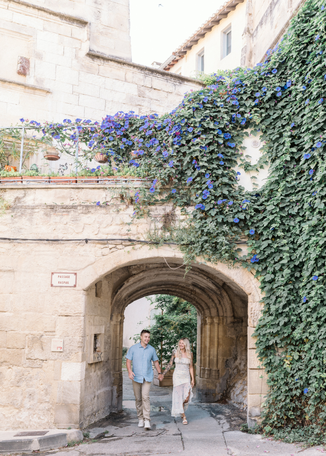 young engaged couple walk through ancient gate in arles france