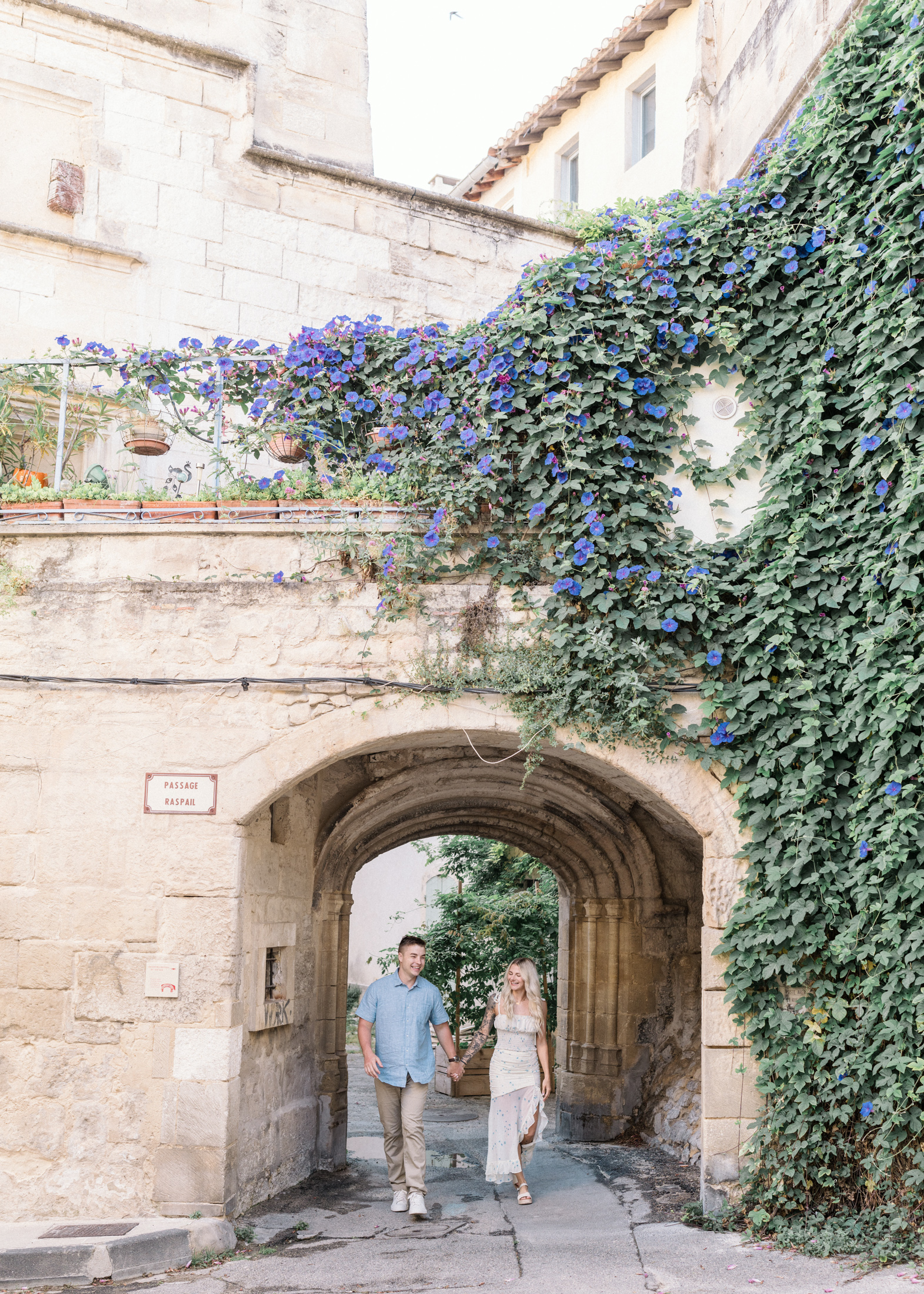 young engaged couple walk through ancient gate in arles france during Engagement Photos In Provence