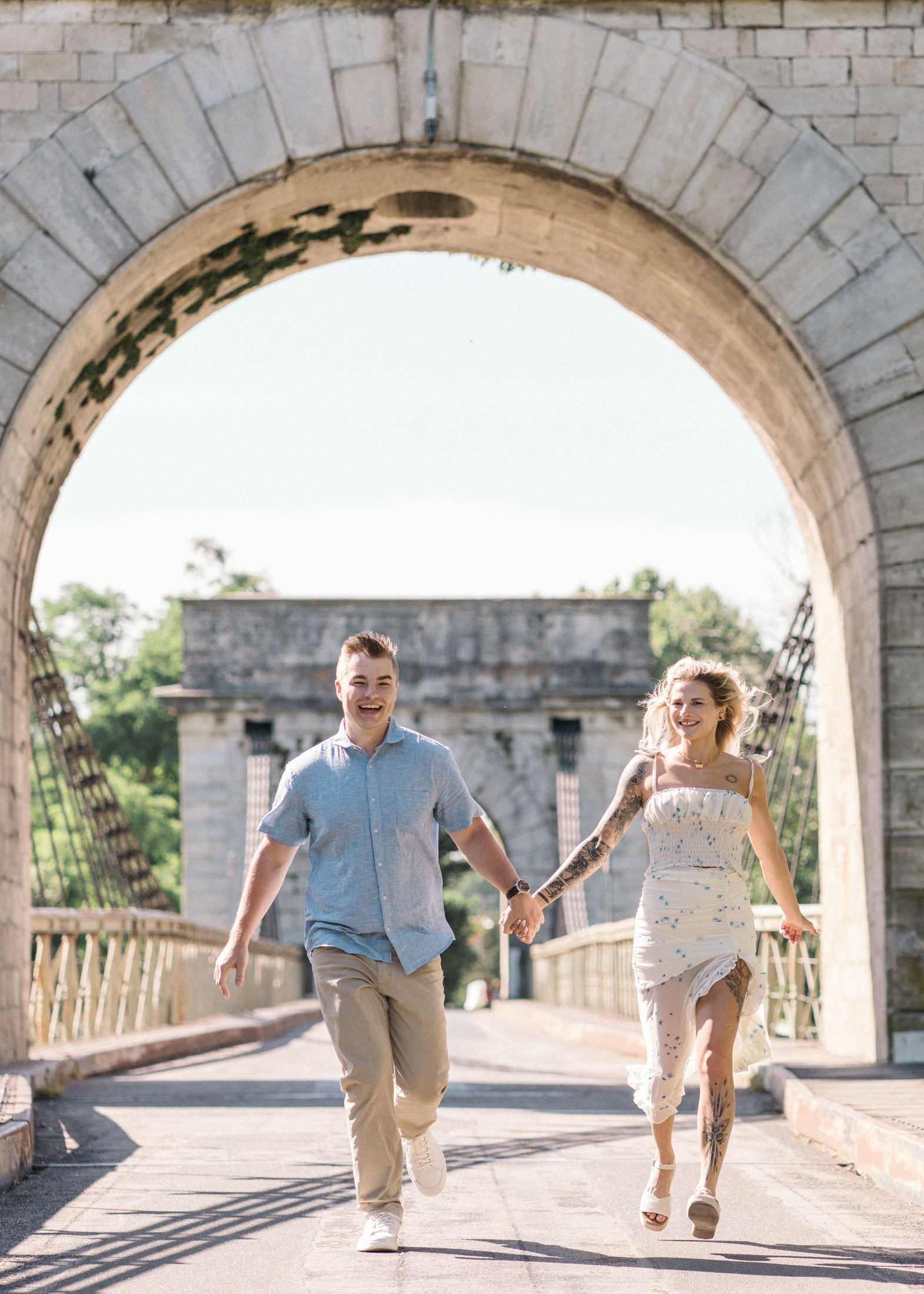 young engaged couple run on stone bridge in arles france