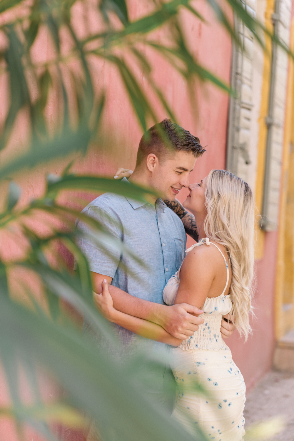 young engaged couple embrace next to pink building in arles france