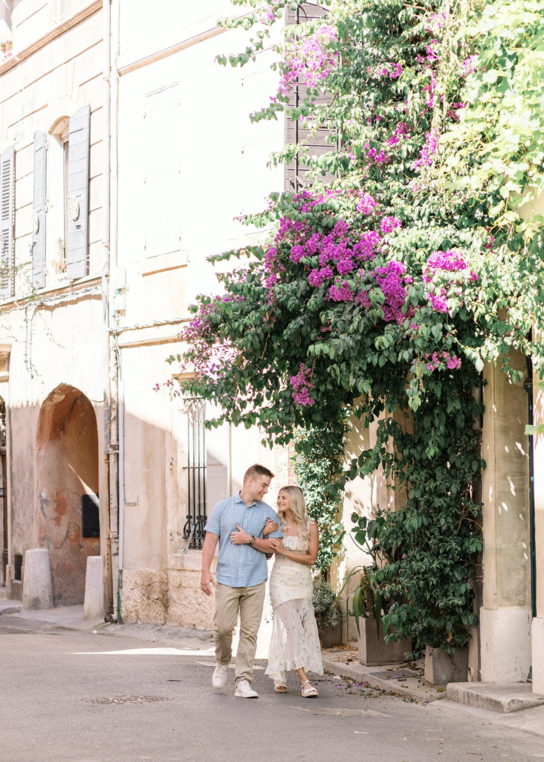 young engaged couple walk arm in arm under bougainvillea tree in arles france