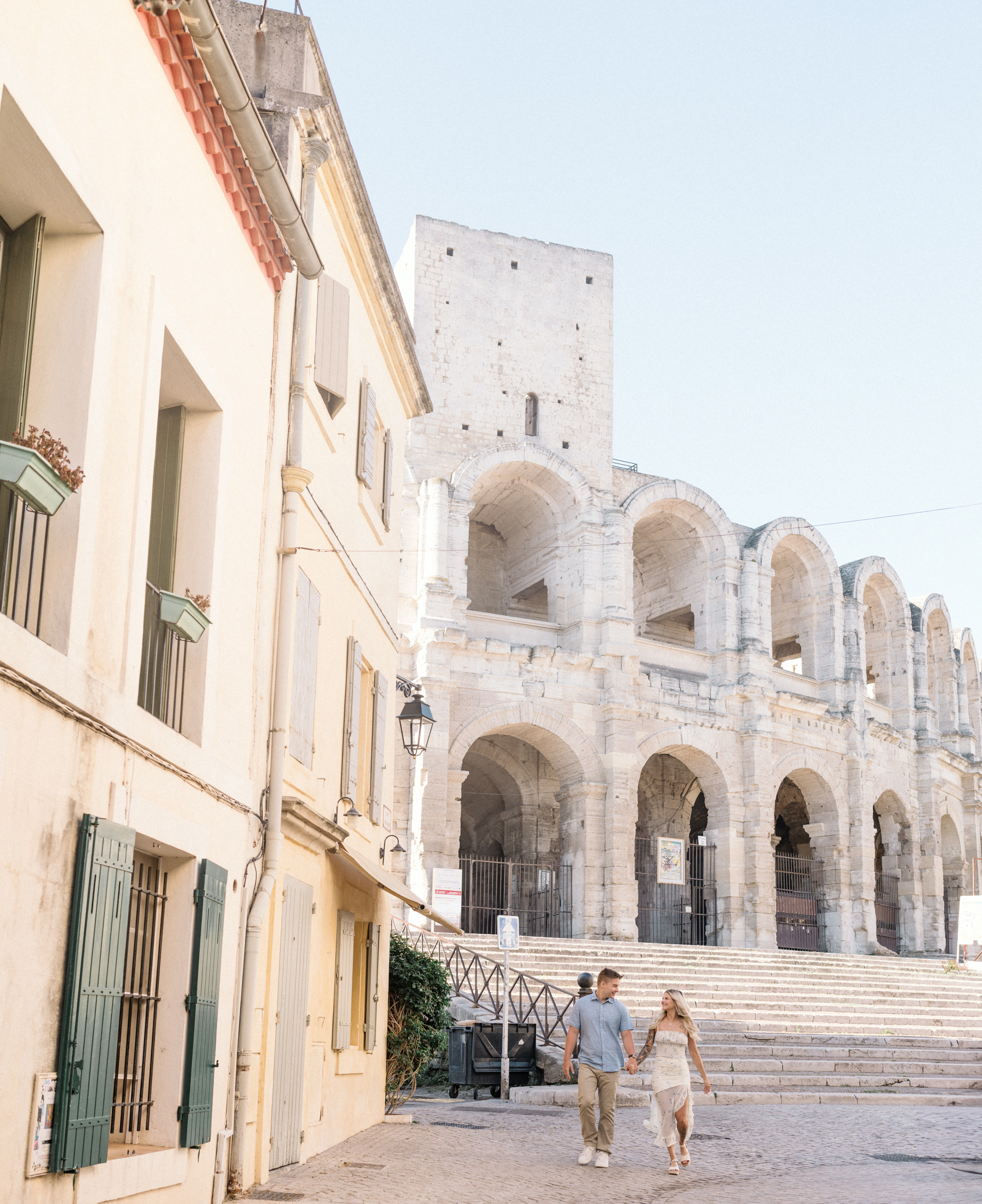 young engaged couple walk hand in hand with arles amphitheatre in background