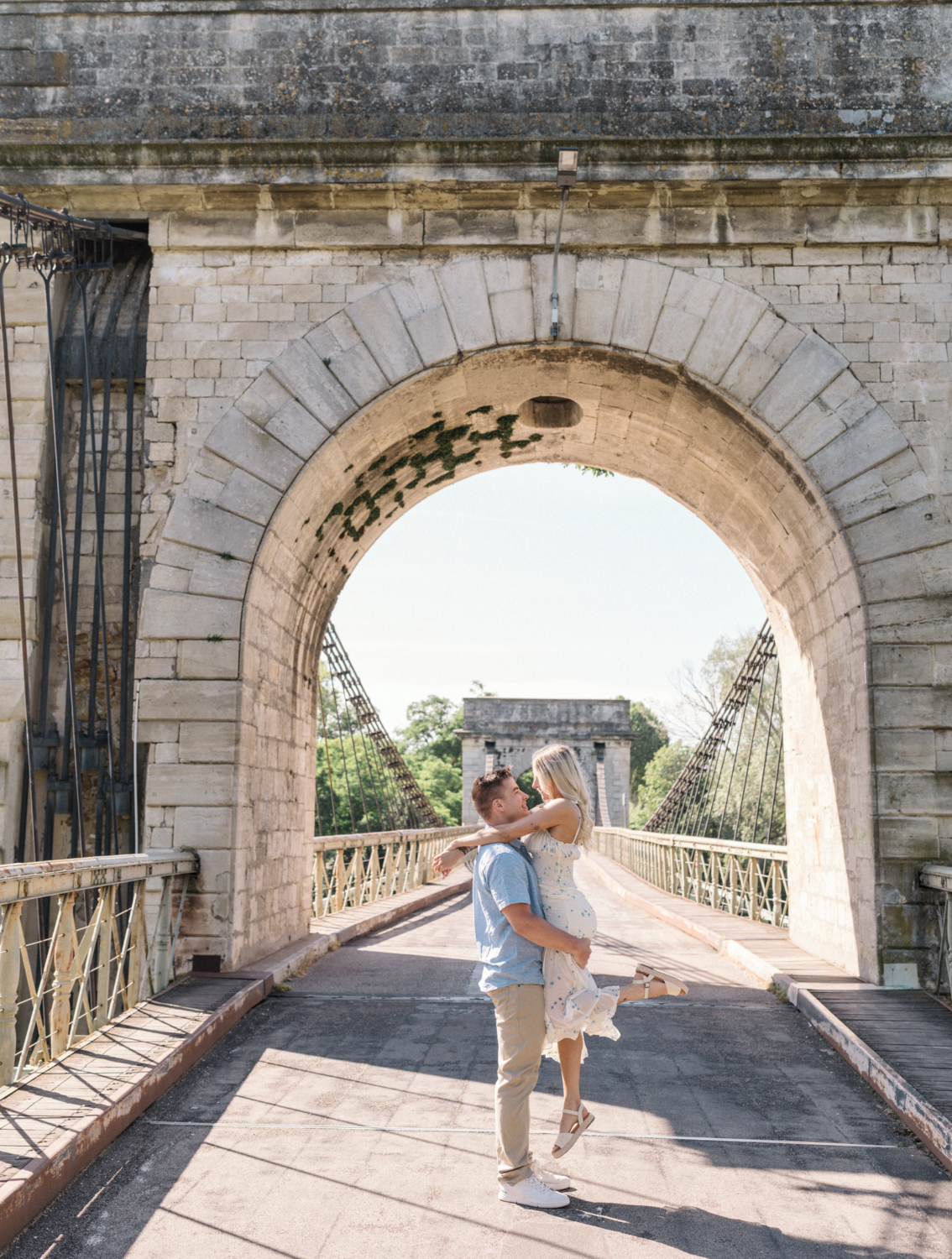 man lifts woman in air on old stone bridge in arles france