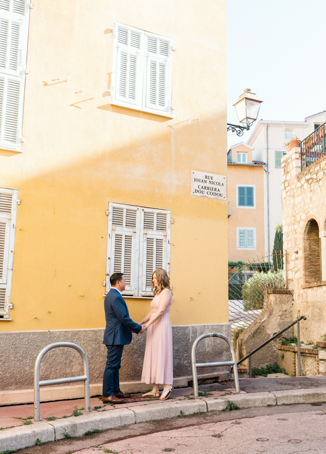 man and woman hold hands in front of yellow building in nice, france